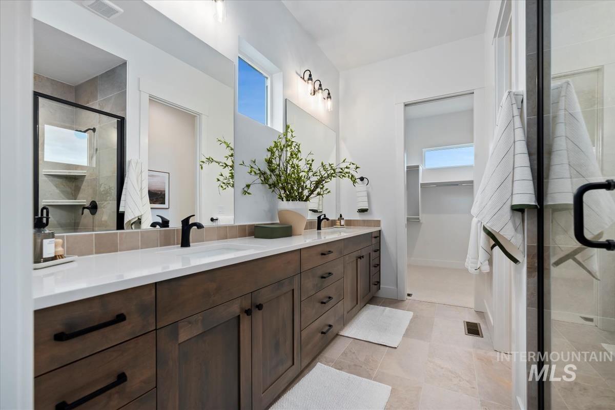 Full bath featuring double vanity, a stall shower, and a walk in closet