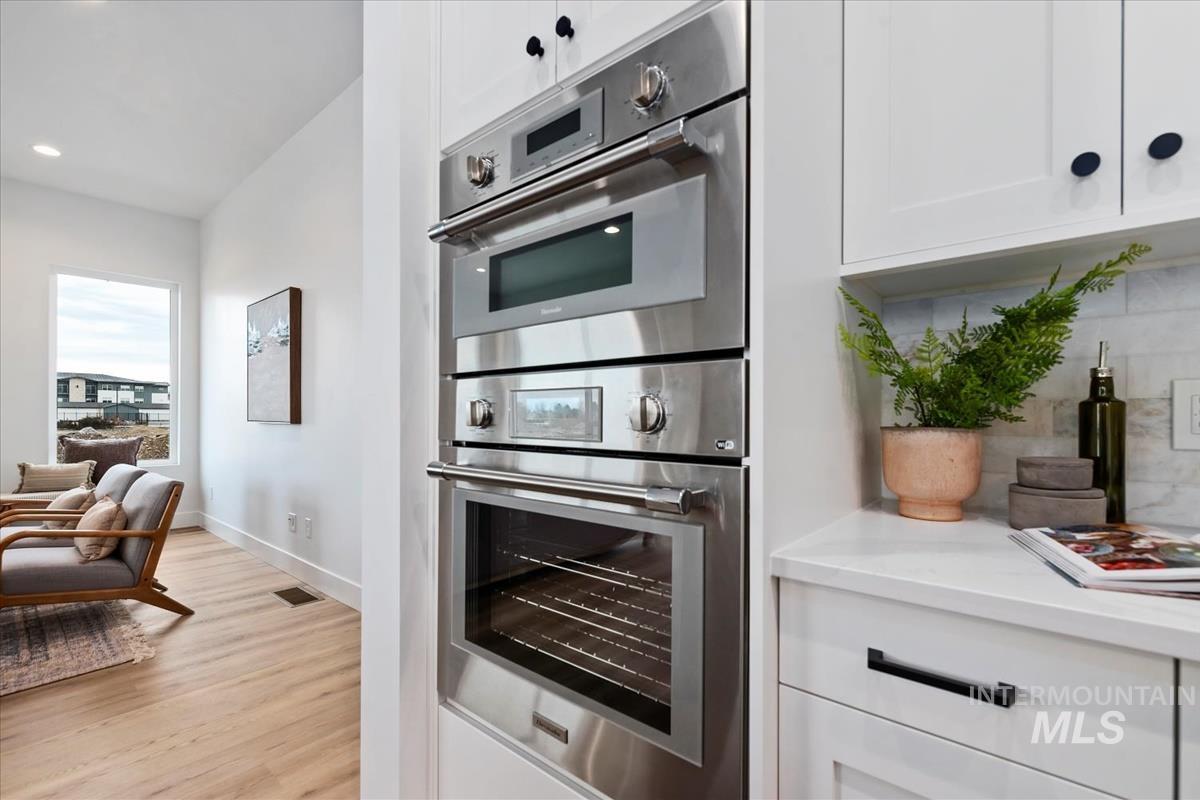Kitchen with stainless steel double oven, white cabinets, tasteful backsplash, light stone counters, and recessed lighting