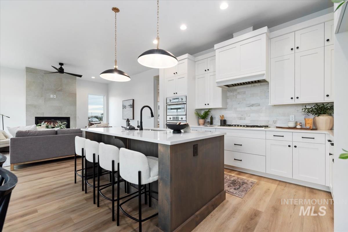 Kitchen featuring white cabinetry, a kitchen breakfast bar, an island with sink, a tiled fireplace, and dark brown cabinetry