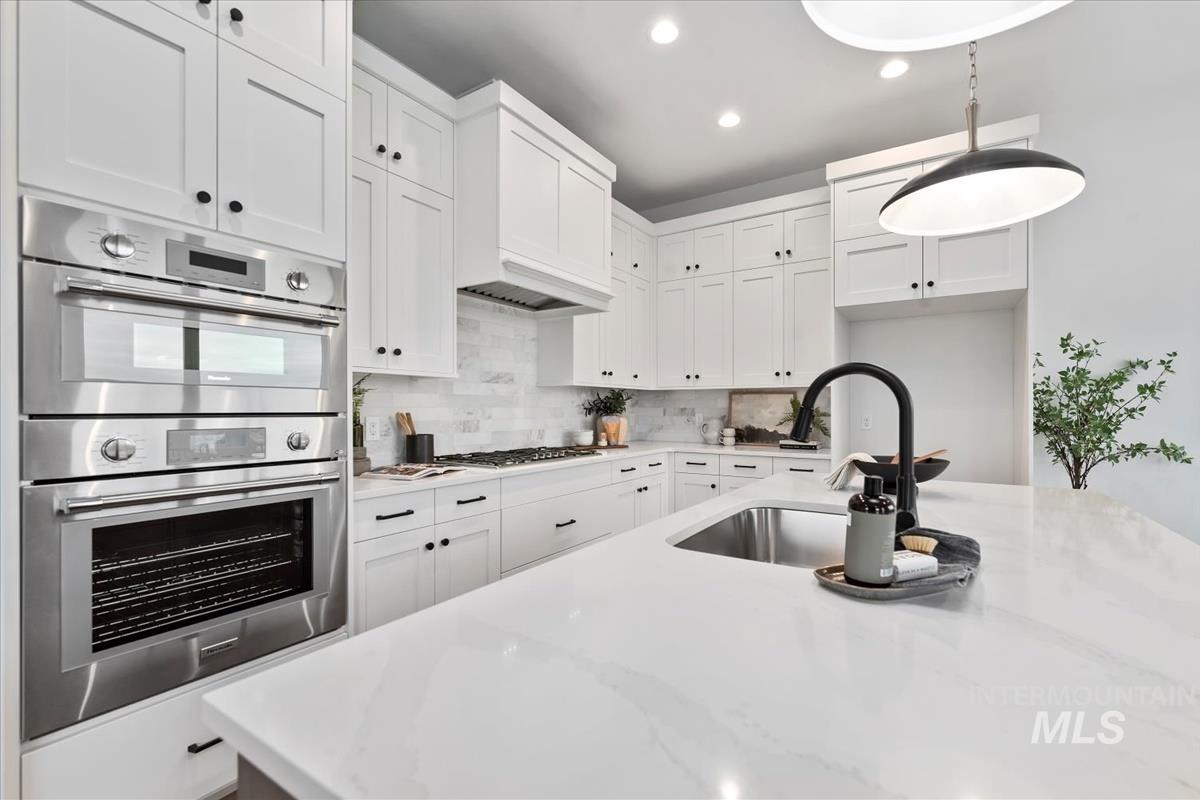 Kitchen with stainless steel appliances, light stone countertops, white cabinets, recessed lighting, and backsplash