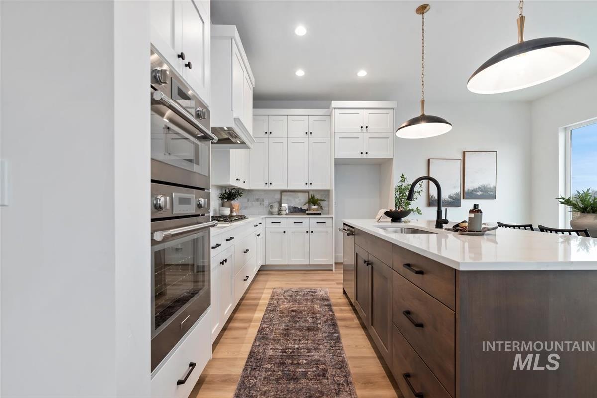 Kitchen featuring white cabinetry, recessed lighting, stainless steel appliances, decorative light fixtures, and light stone counters