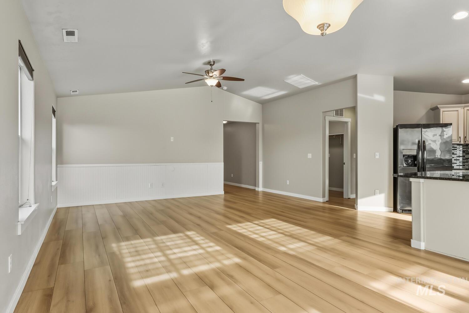 Unfurnished living room featuring light wood-style flooring, ceiling fan, wainscoting, and vaulted ceiling