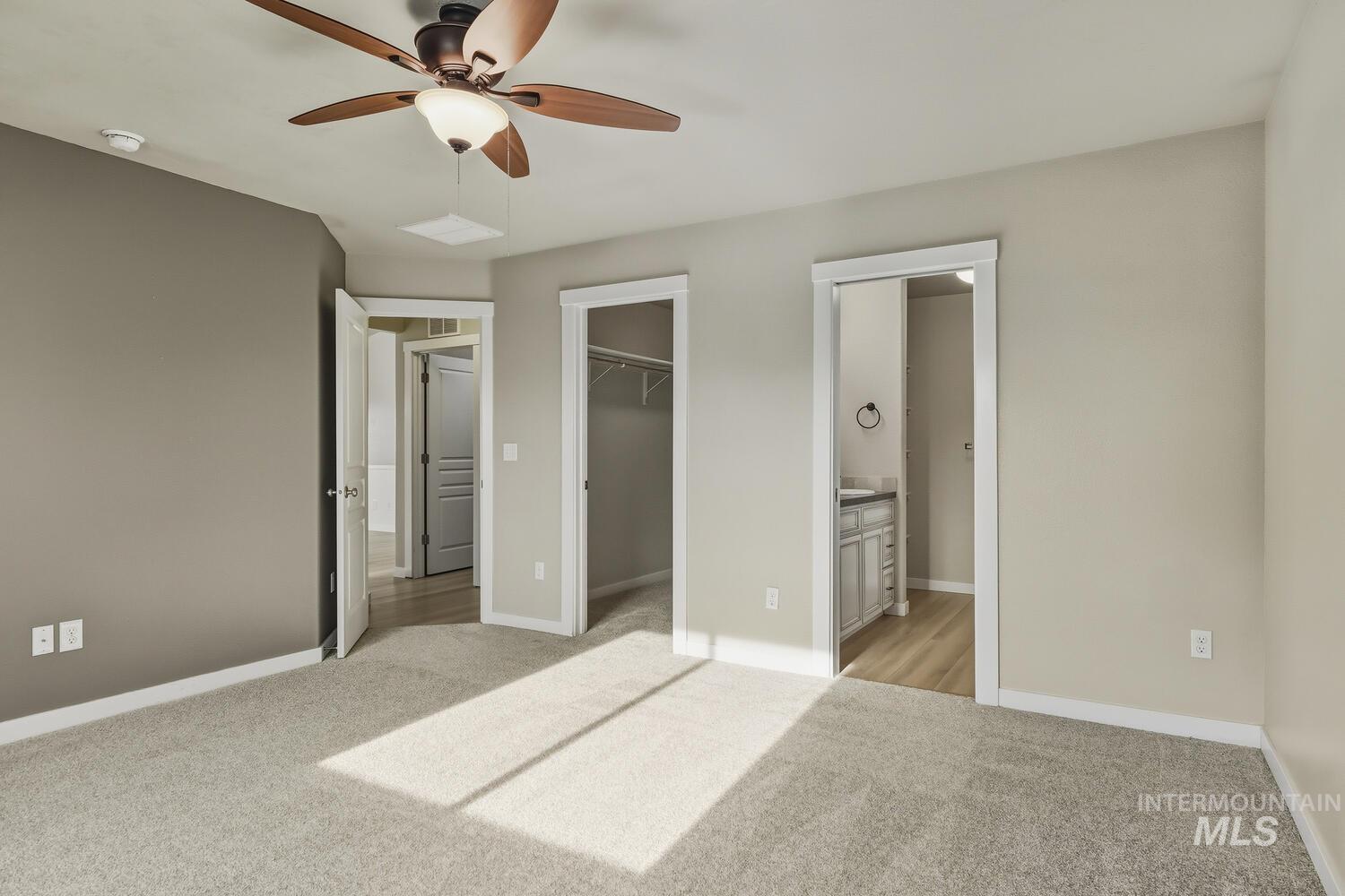 Unfurnished bedroom with light colored carpet, a walk in closet, a ceiling fan, and ensuite bathroom