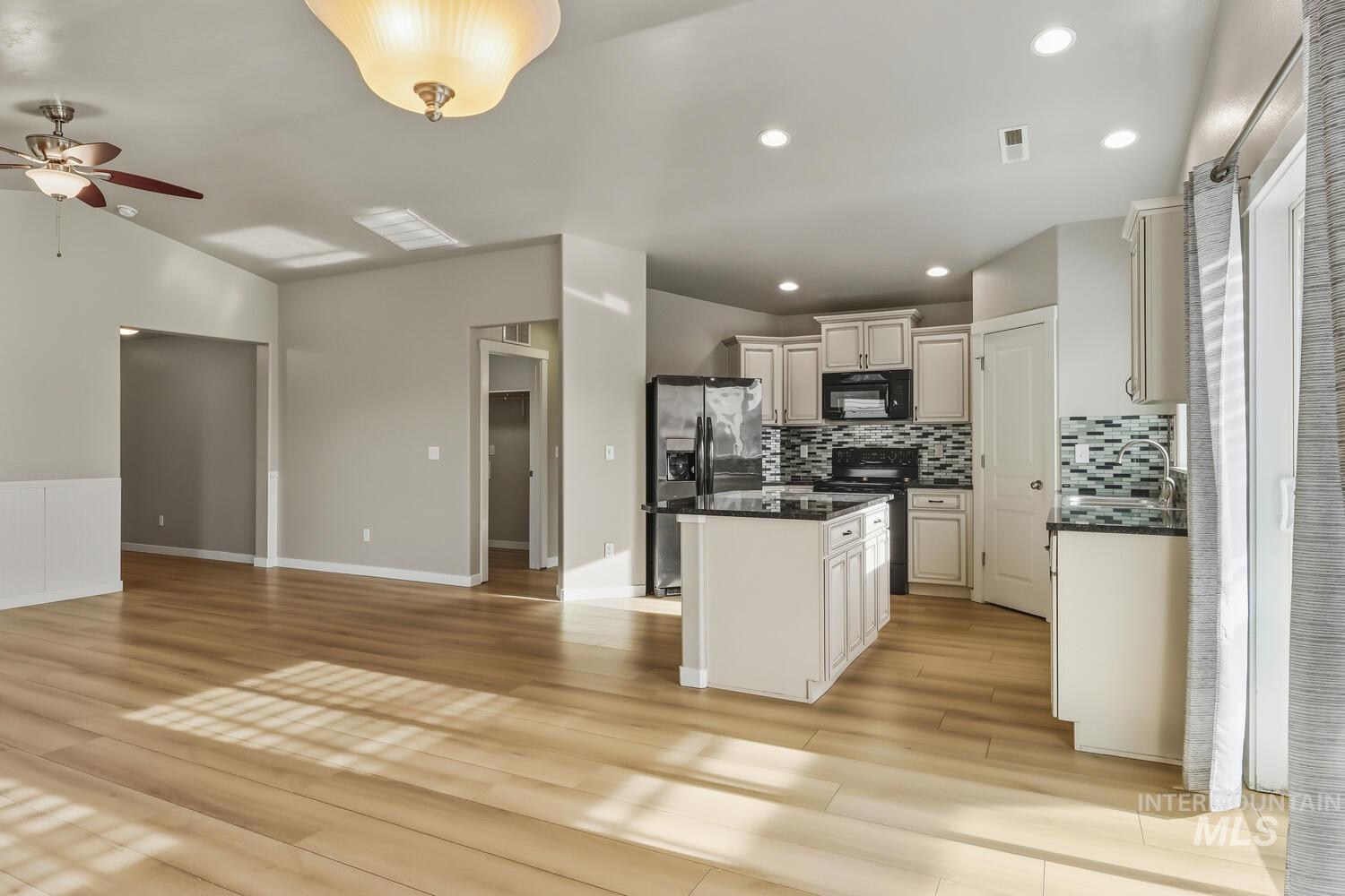 Kitchen with open floor plan, backsplash, stainless steel appliances, a center island, and light wood finished floors