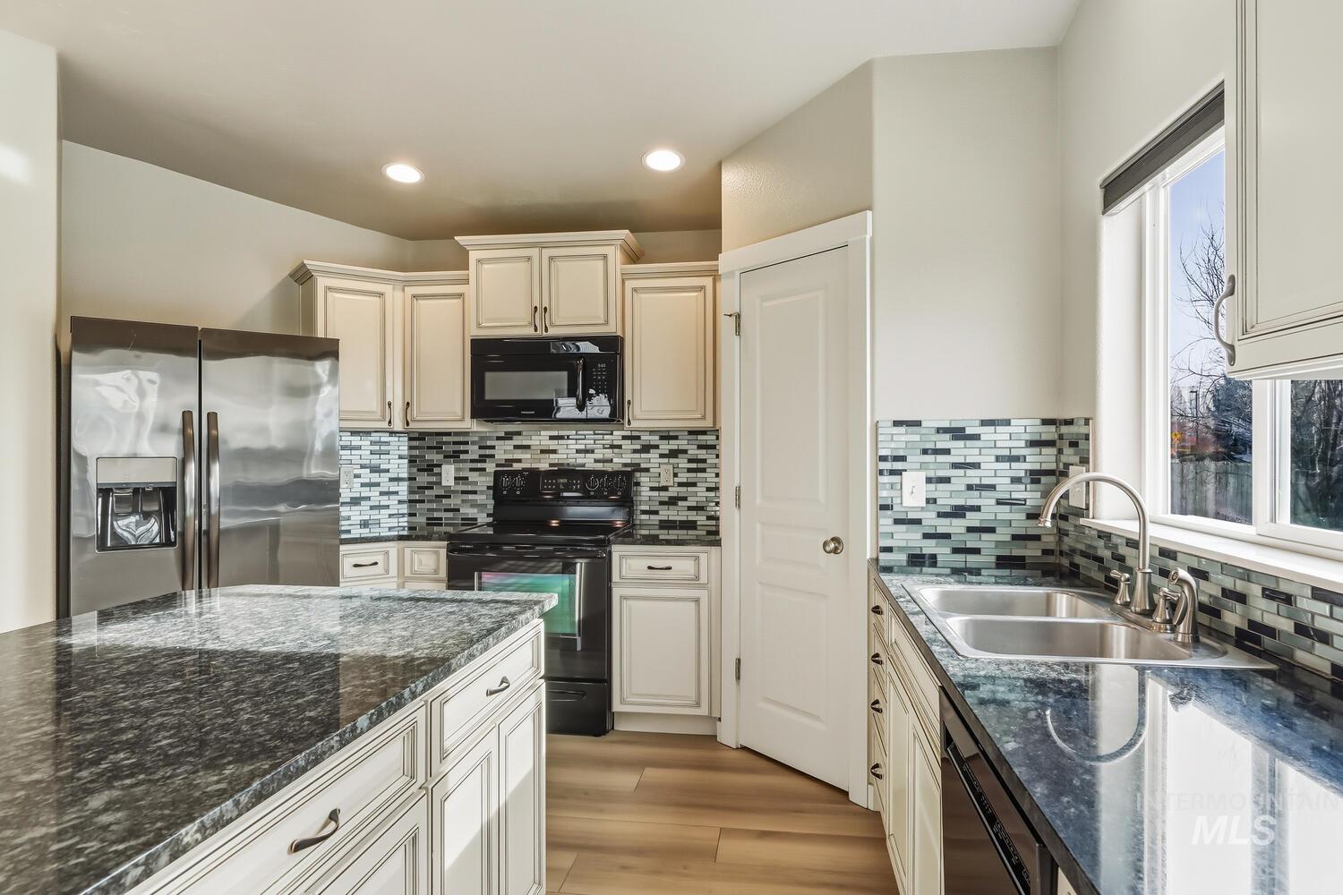 Kitchen with dark stone countertops, black appliances, light wood finished floors, cream cabinets, and recessed lighting