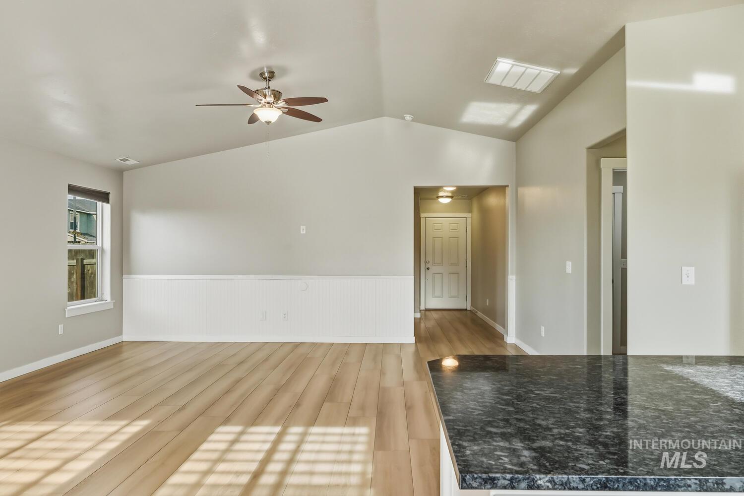 Empty room featuring light wood-style flooring, a ceiling fan, a wainscoted wall, and lofted ceiling