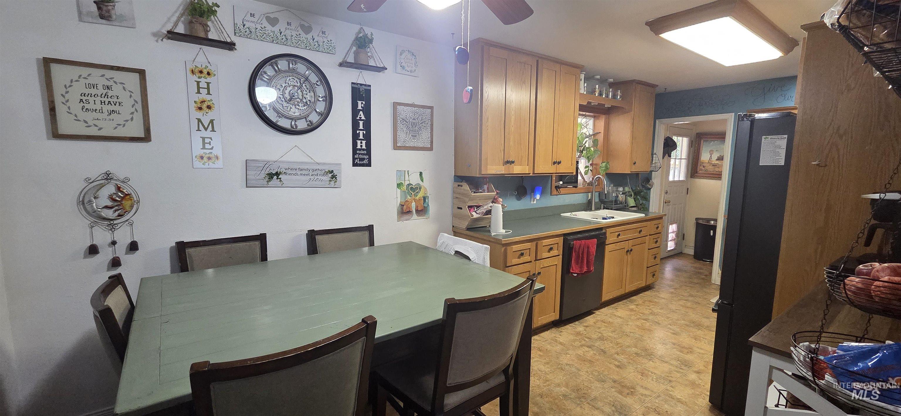 Kitchen with stainless steel dishwasher, ceiling fan, freestanding refrigerator, light flooring, and dark countertops