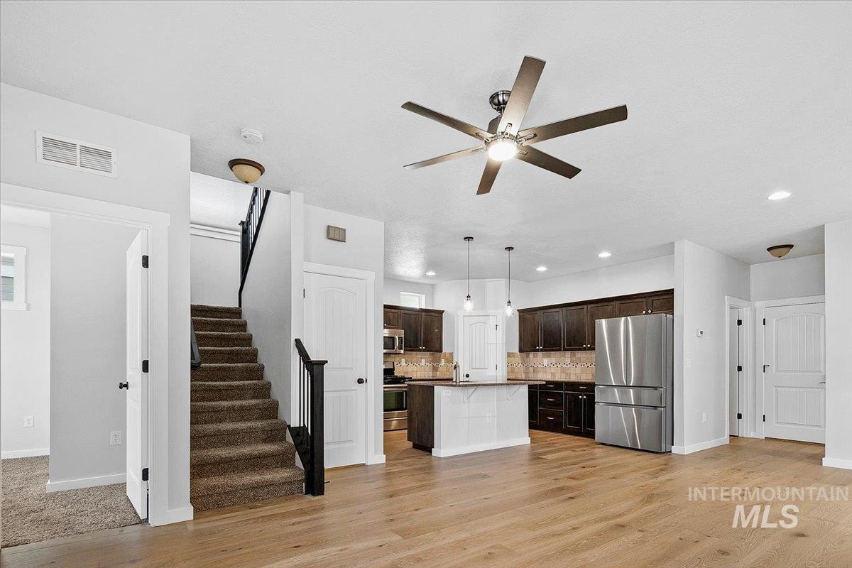 Kitchen featuring dark wood finish cabinets, decorative backsplash, stainless steel appliances, a kitchen island, and light wood-style flooring