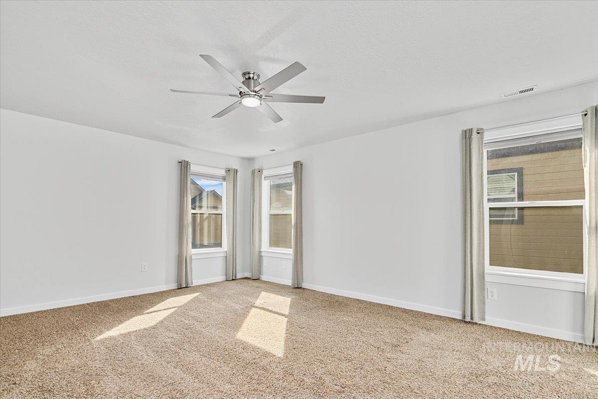Empty room with light colored carpet, a ceiling fan, a textured ceiling, and healthy amount of natural light