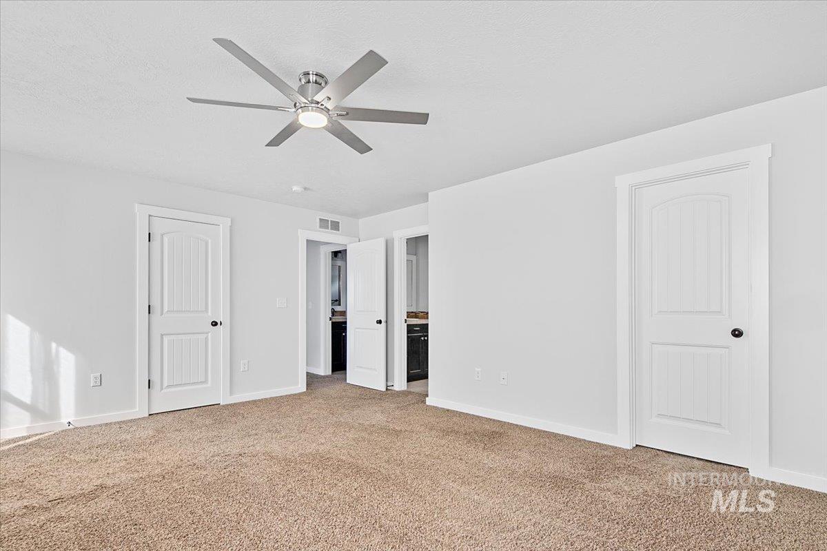 Unfurnished bedroom with ensuite bathroom, light colored carpet, and ceiling fan
