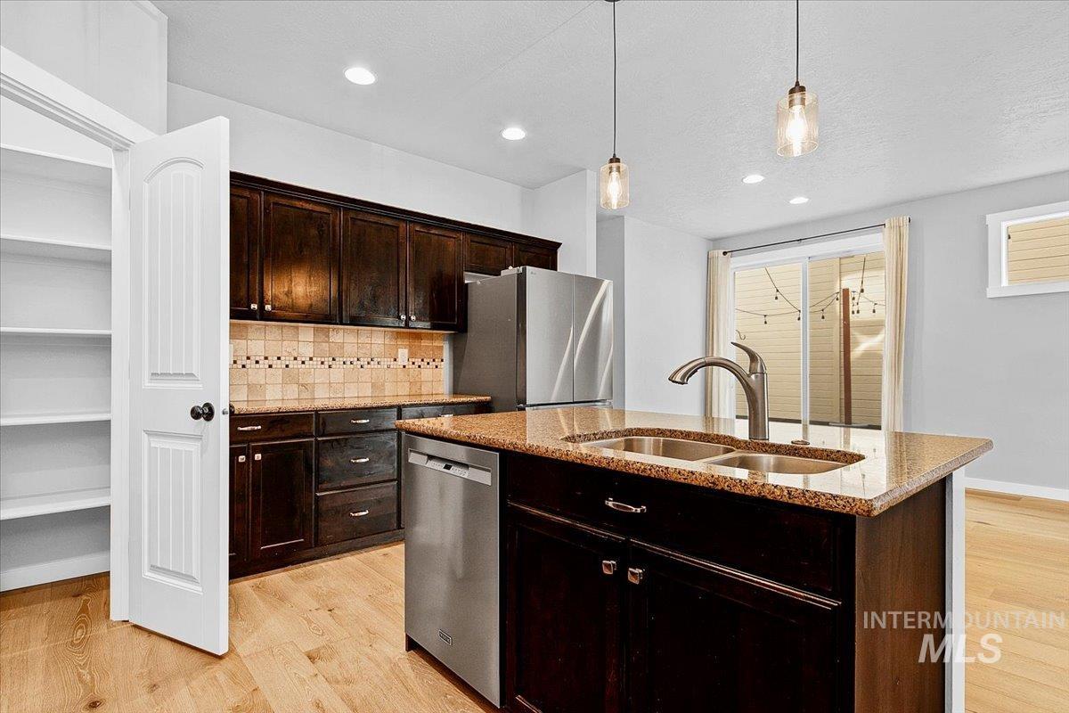 Kitchen with dark wood finish cabinets, light wood-style floors, light stone countertops, decorative backsplash, and a textured ceiling