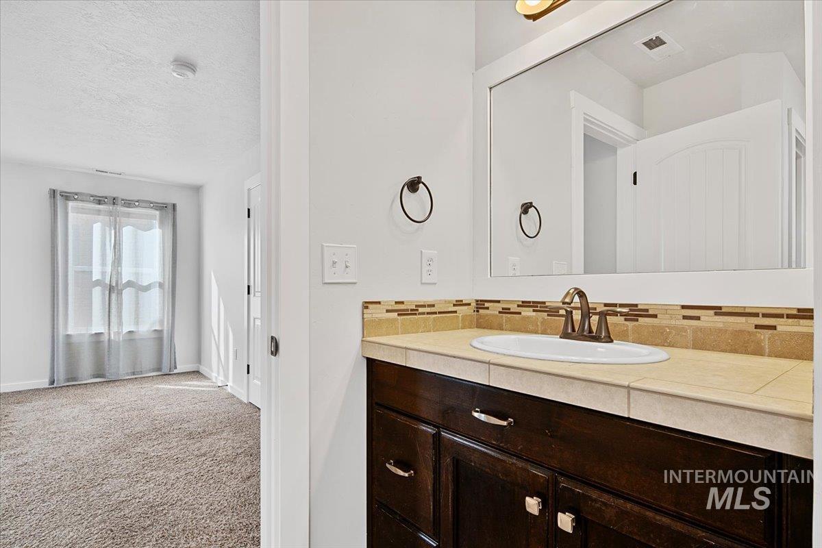 Bathroom featuring vanity, tasteful backsplash, light carpet, and a textured ceiling