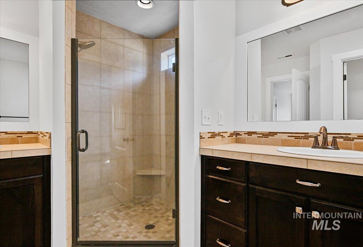 Full bathroom featuring vanity, a shower stall, and decorative backsplash