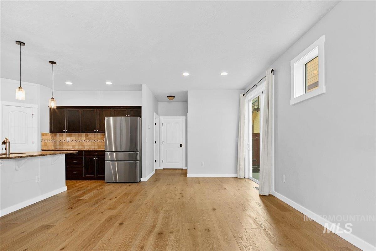 Kitchen with dark wood finish cabinetry, freestanding refrigerator, dark stone countertops, light wood finished floors, and hanging light fixtures