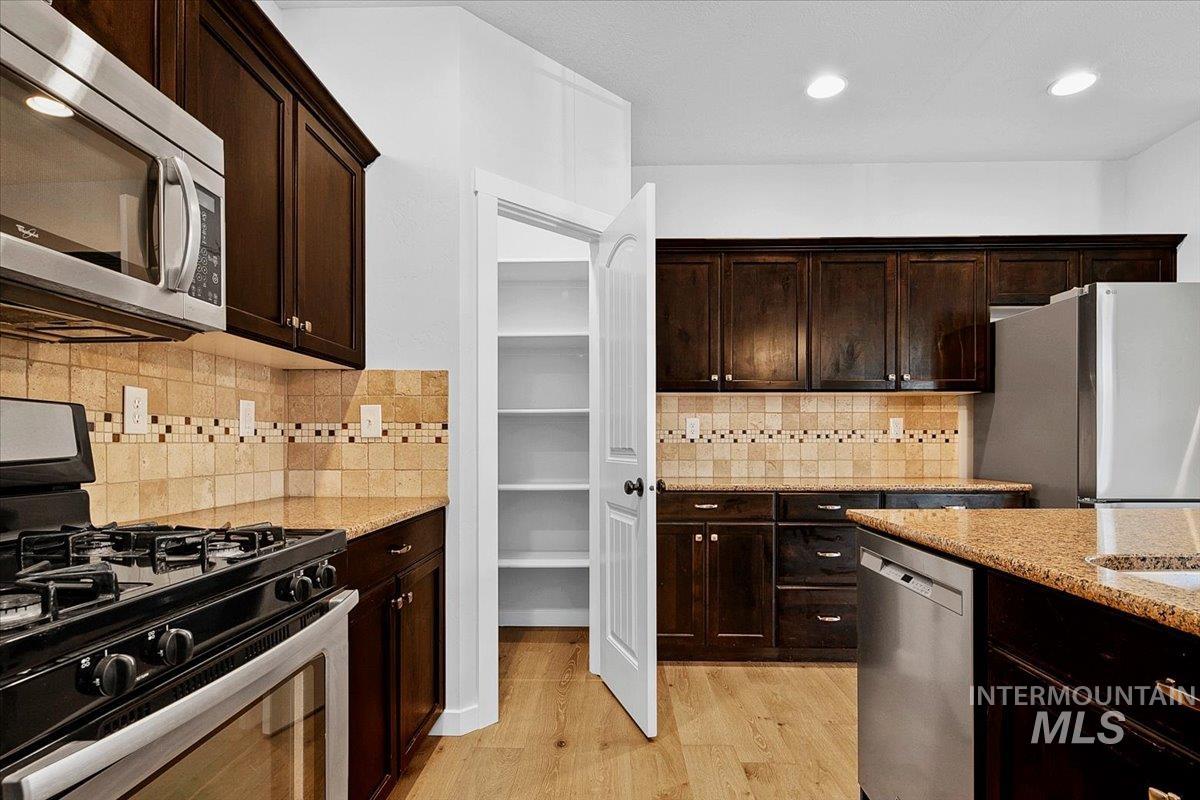 Kitchen featuring dark wood finish cabinetry, stainless steel appliances, light stone counters, light wood finished floors, and recessed lighting