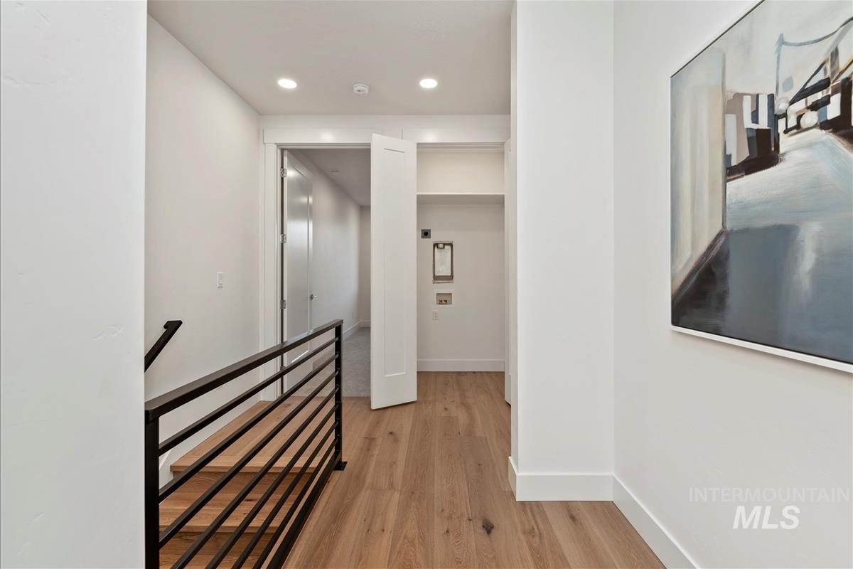 Hallway featuring light wood finished floors, an upstairs landing, and recessed lighting