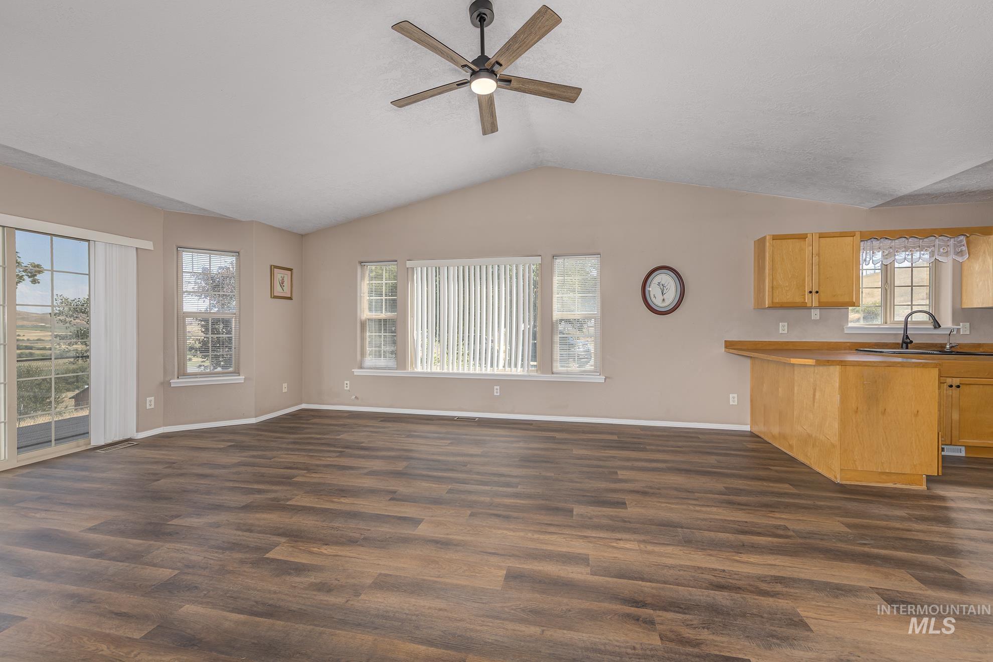 Unfurnished living room featuring dark wood-style floors, lofted ceiling, and a ceiling fan