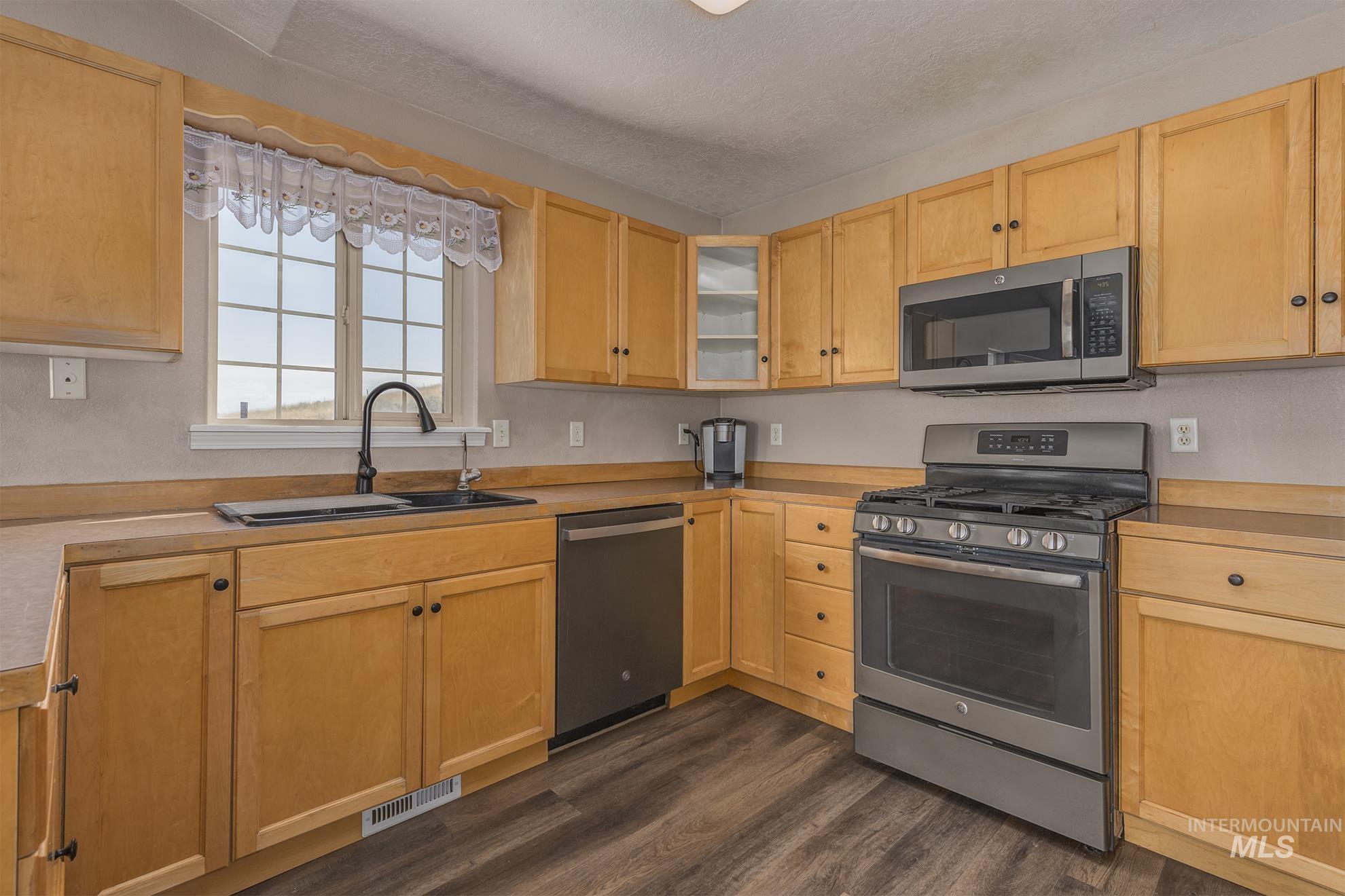 Kitchen with stainless steel appliances, light countertops, dark wood-style floors, light brown cabinetry, and a textured ceiling