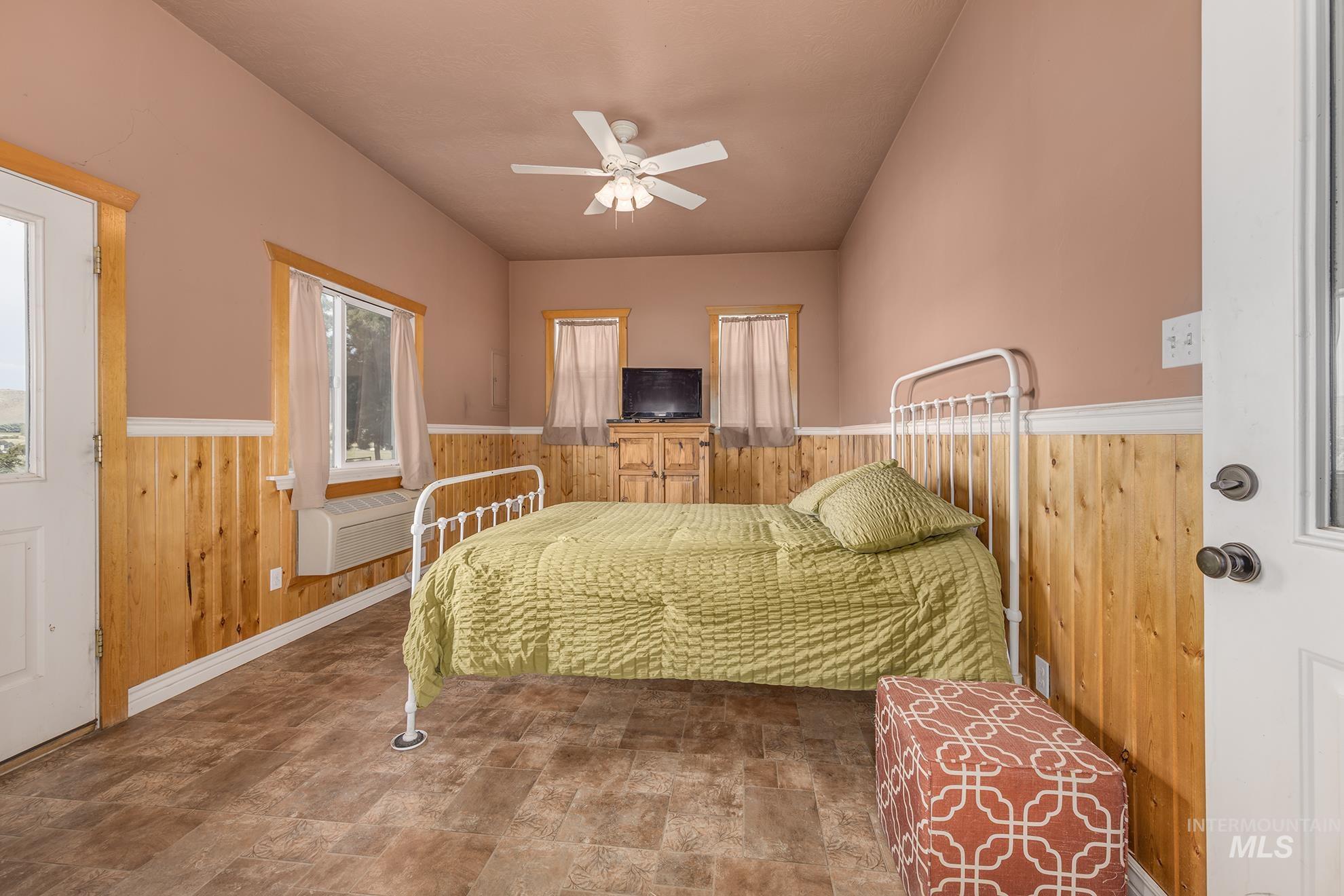 Bedroom with wood walls, a wainscoted wall, a ceiling fan, and stone finish flooring