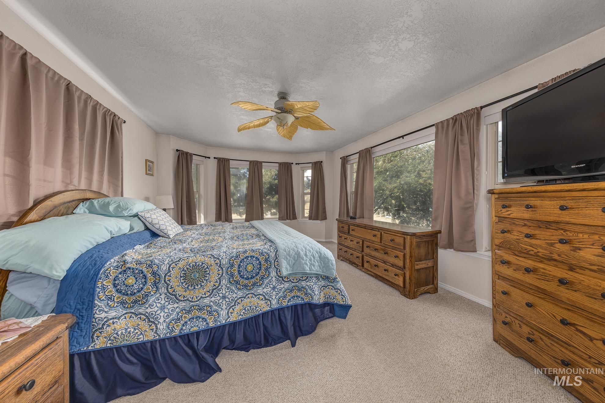 Bedroom featuring multiple windows, a textured ceiling, light carpet, and ceiling fan
