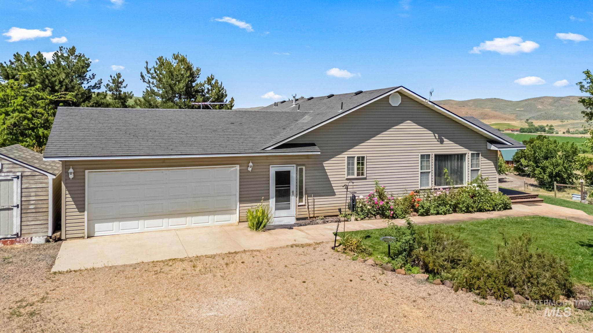 Ranch-style home featuring a garage, driveway, a mountain view, a shingled roof, and a shed