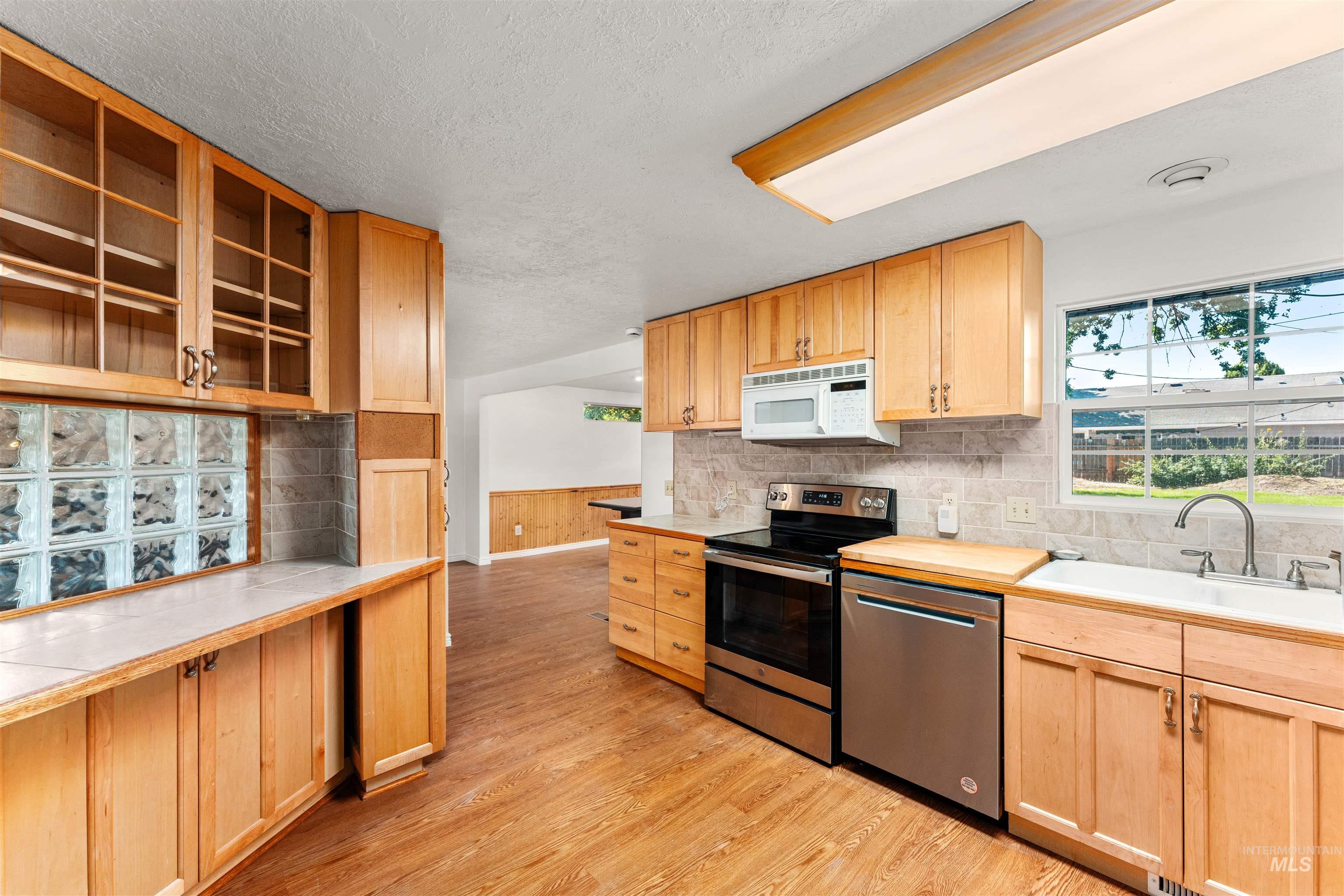 Kitchen with stainless steel appliances, light countertops, light wood finished floors, backsplash, and light brown cabinets