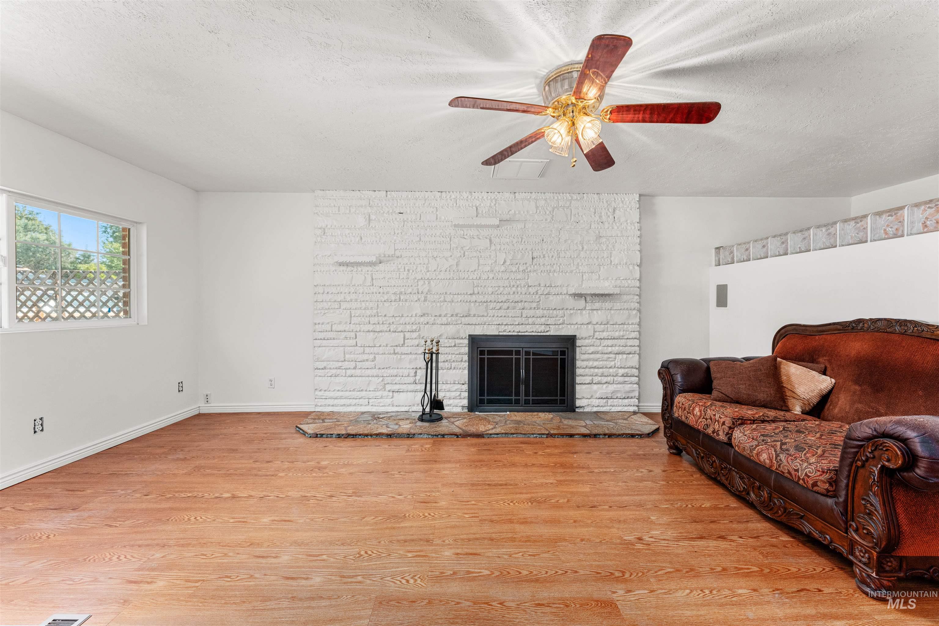 Living area featuring a fireplace, light wood-type flooring, a textured ceiling, and a ceiling fan