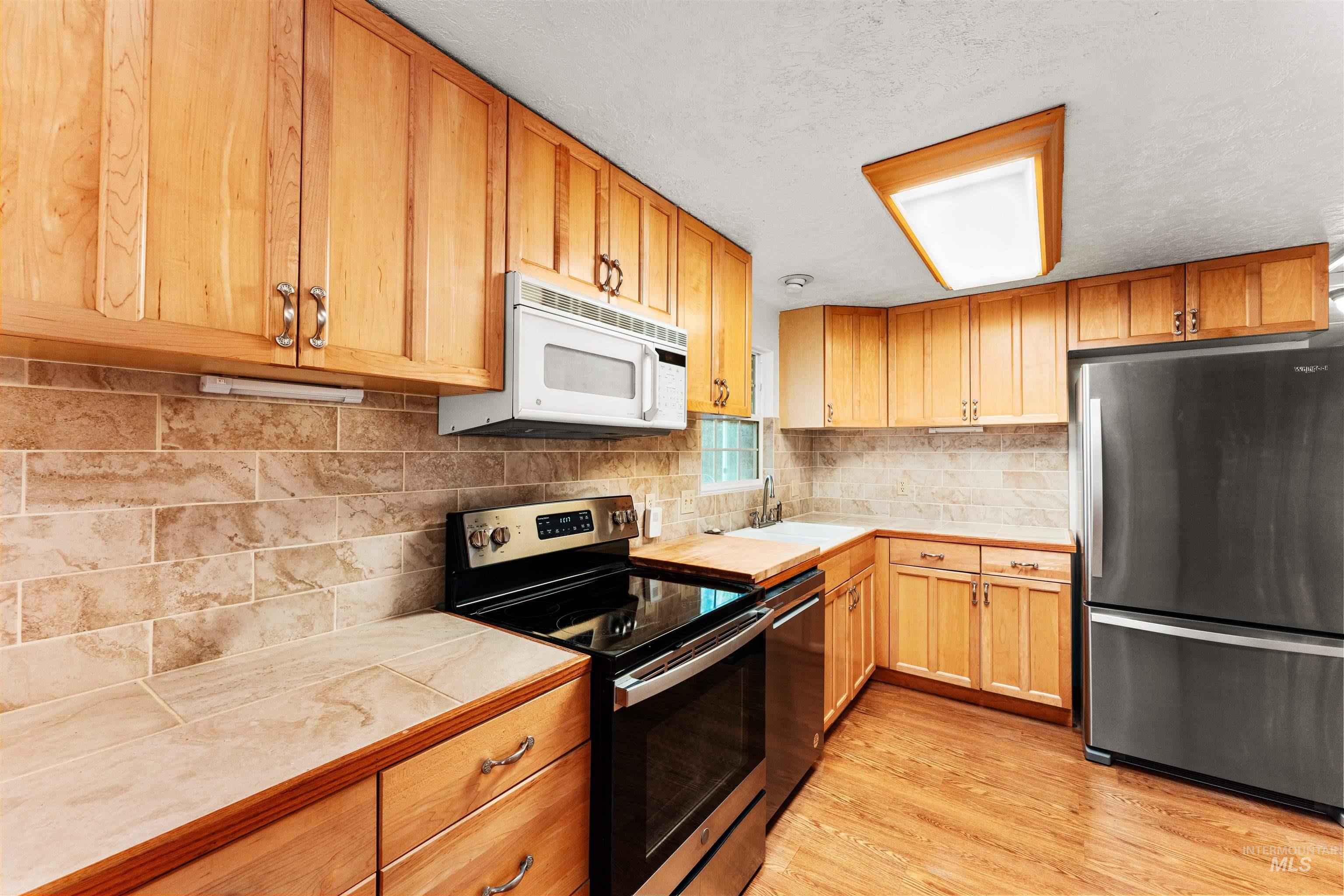 Kitchen featuring appliances with stainless steel finishes, tasteful backsplash, tile counters, light wood-style floors, and a textured ceiling