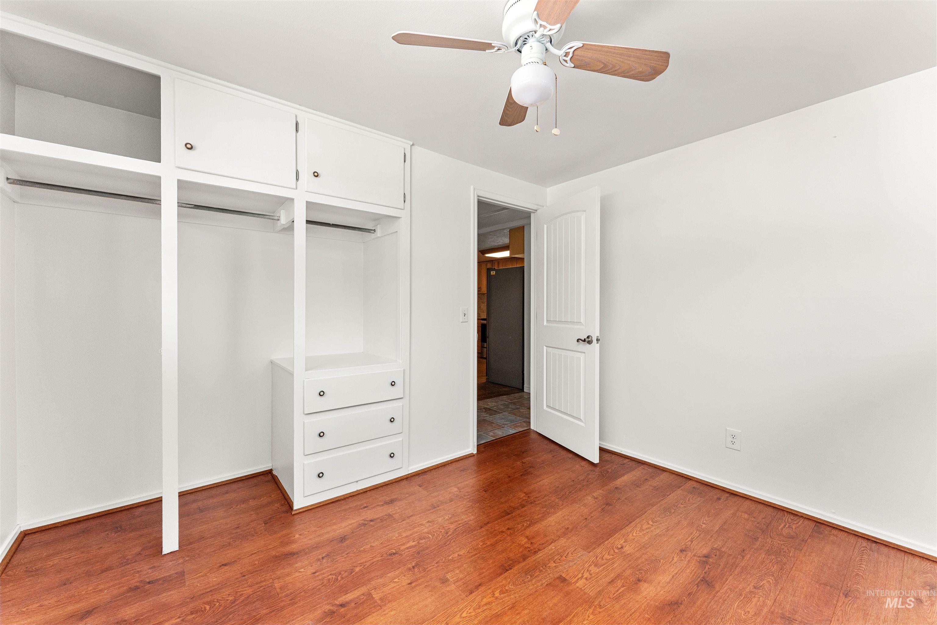 Unfurnished bedroom featuring wood finished floors, a closet, a ceiling fan, and freestanding refrigerator