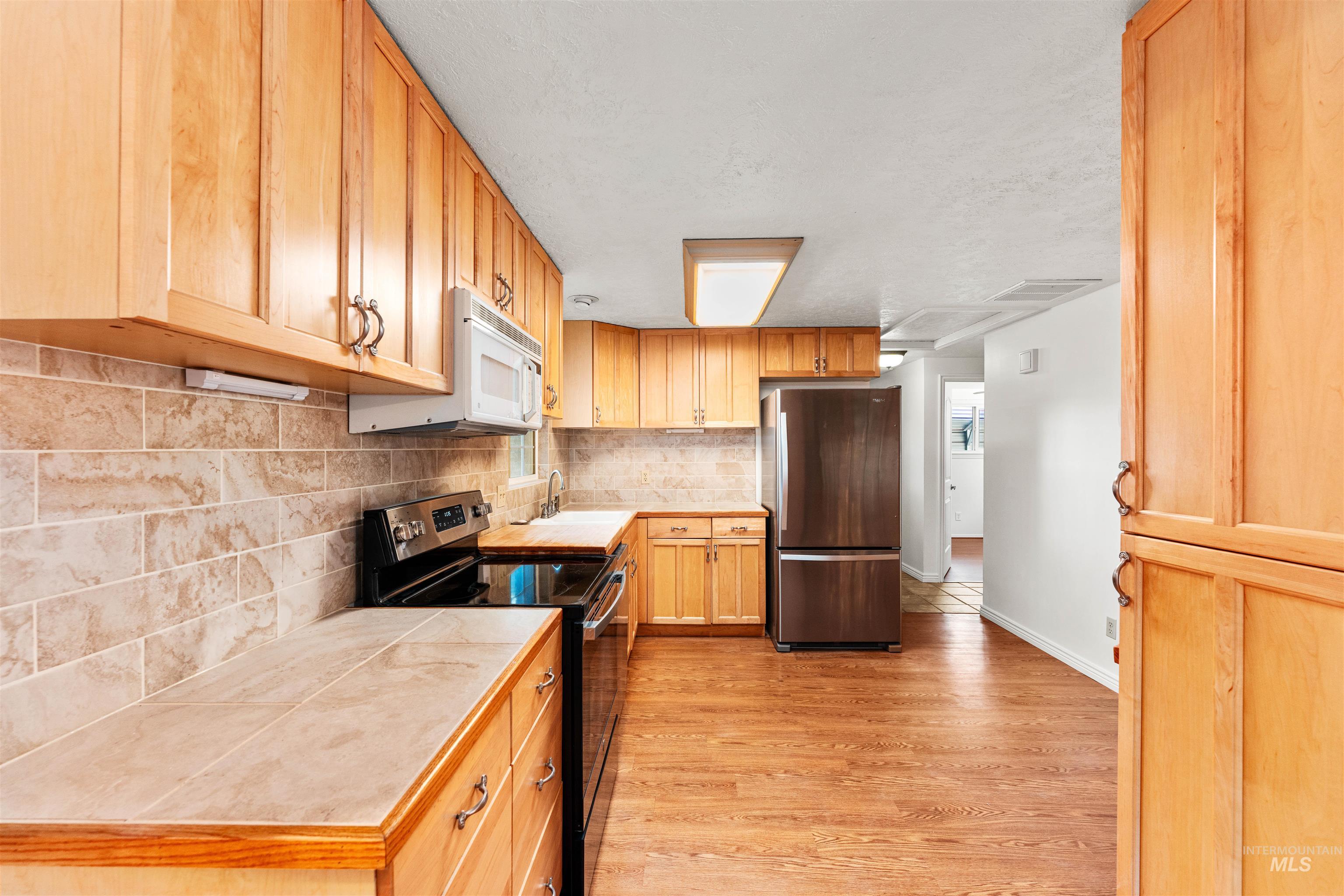 Kitchen featuring stainless steel appliances, tasteful backsplash, light countertops, and light wood-type flooring