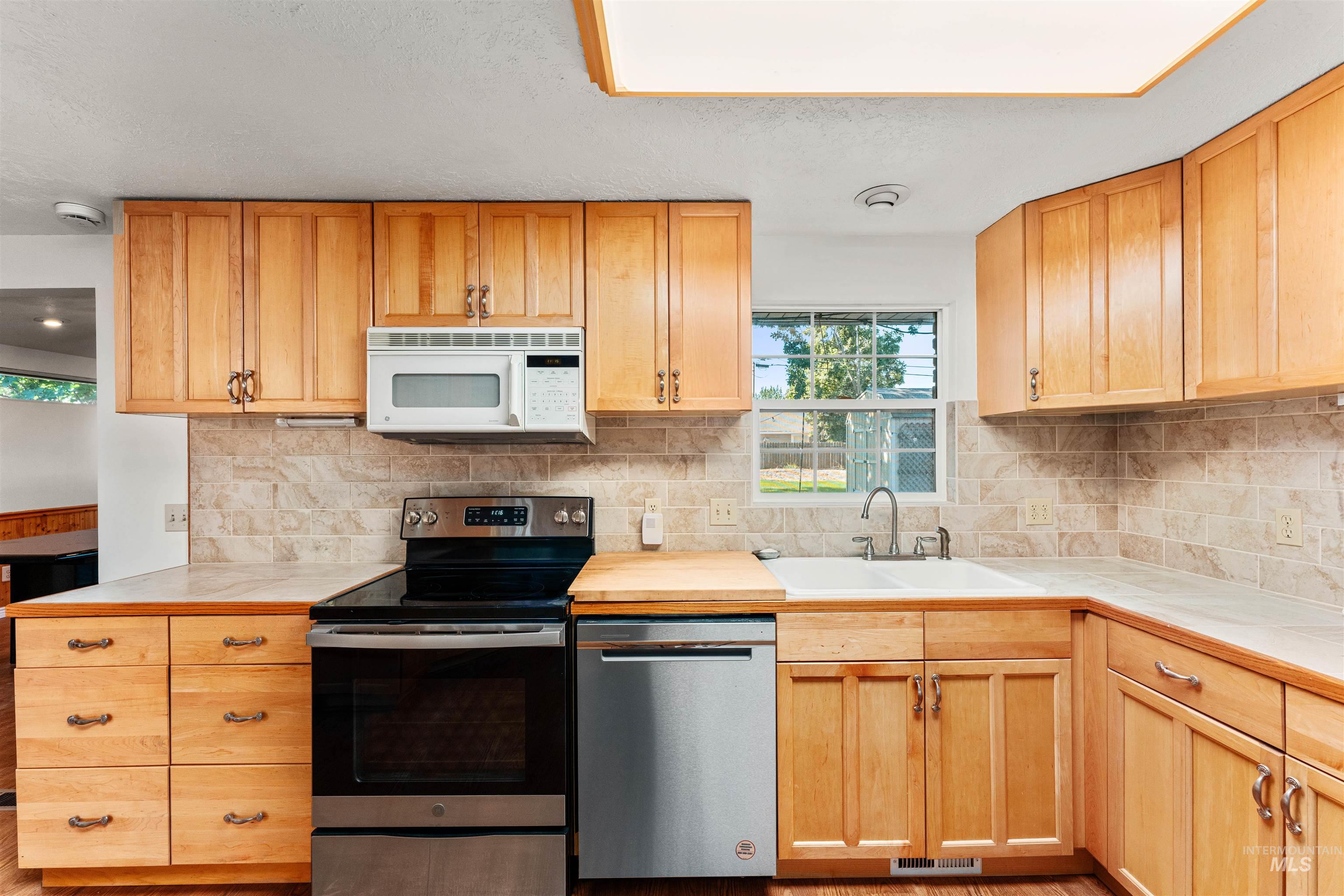 Kitchen featuring appliances with stainless steel finishes, tasteful backsplash, tile counters, and light brown cabinets