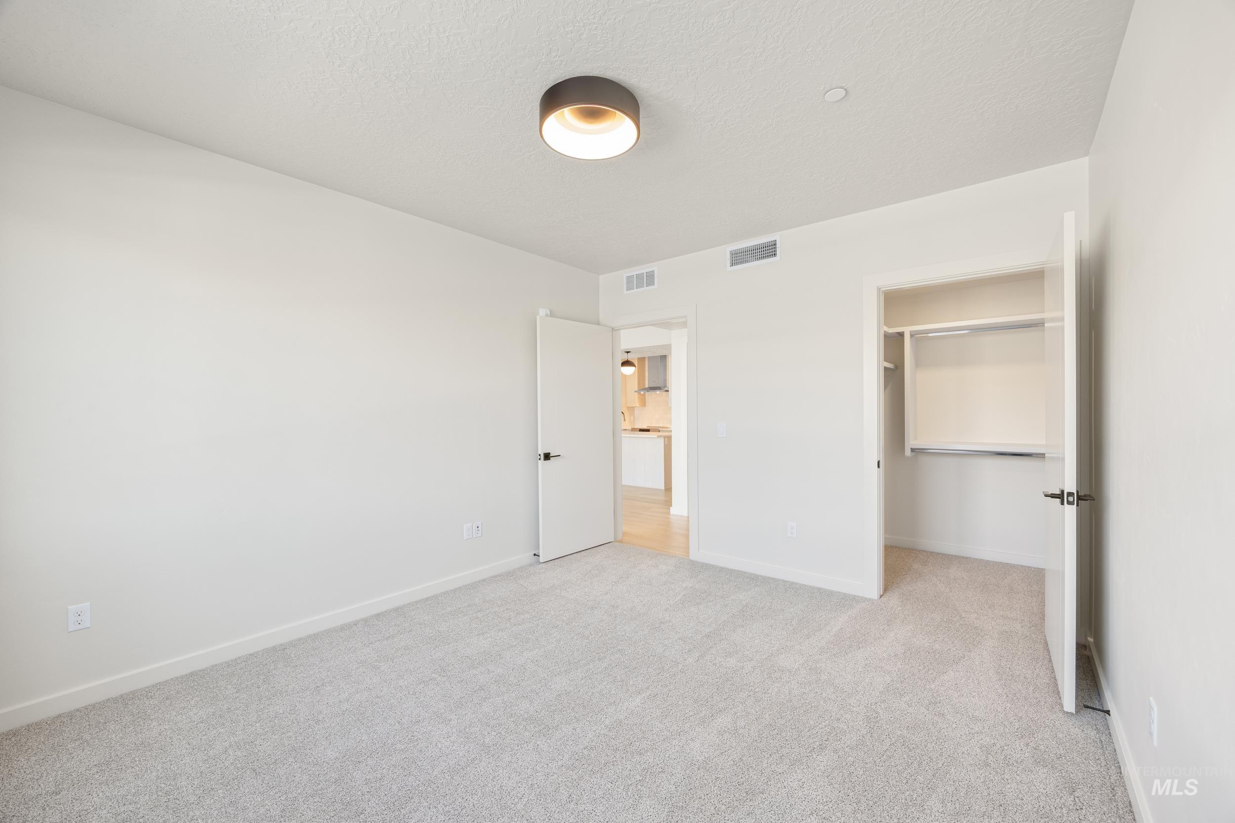 Unfurnished bedroom featuring a walk in closet, light colored carpet, and a textured ceiling