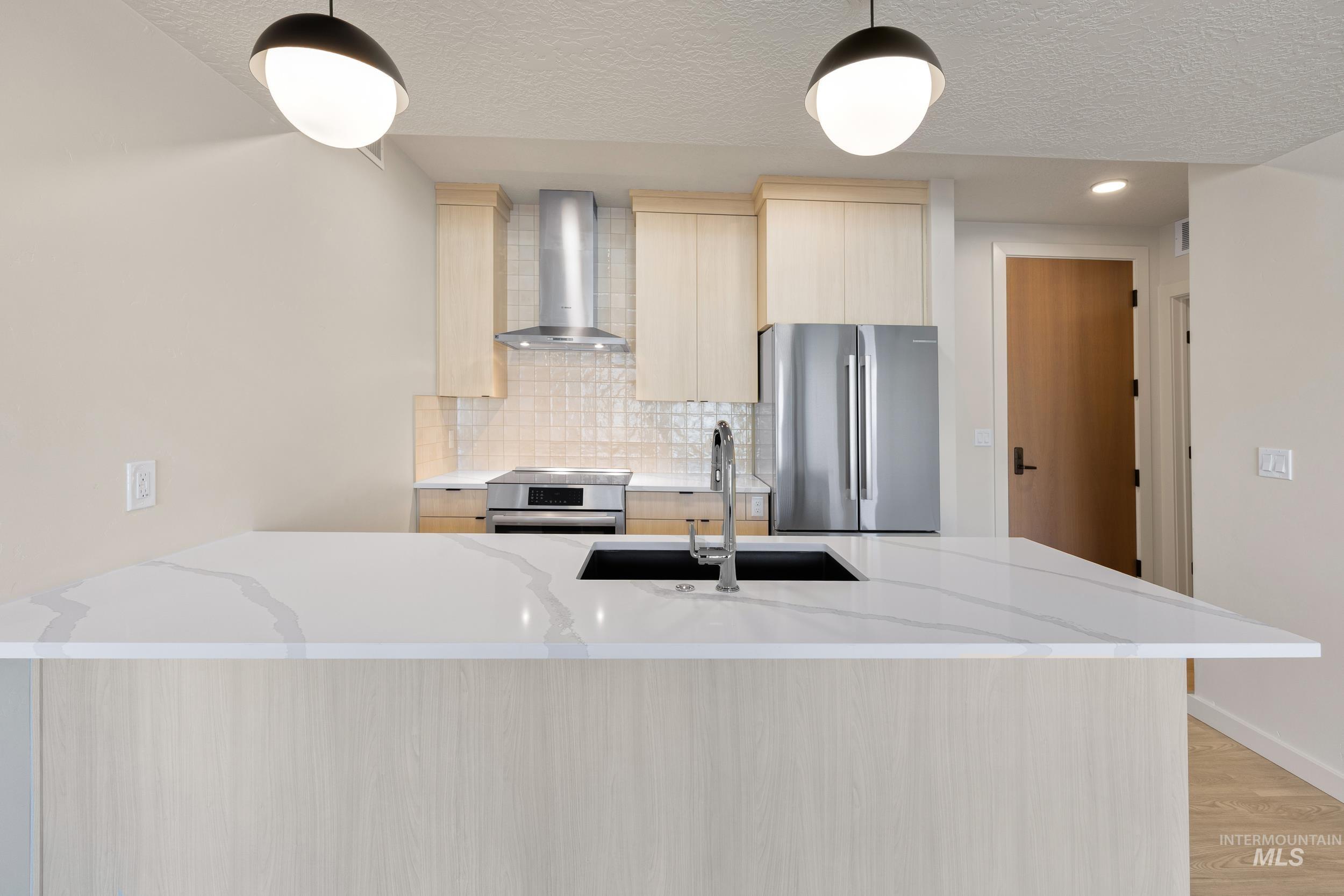Kitchen with light brown cabinetry, light stone countertops, a peninsula, stainless steel appliances, and a textured ceiling