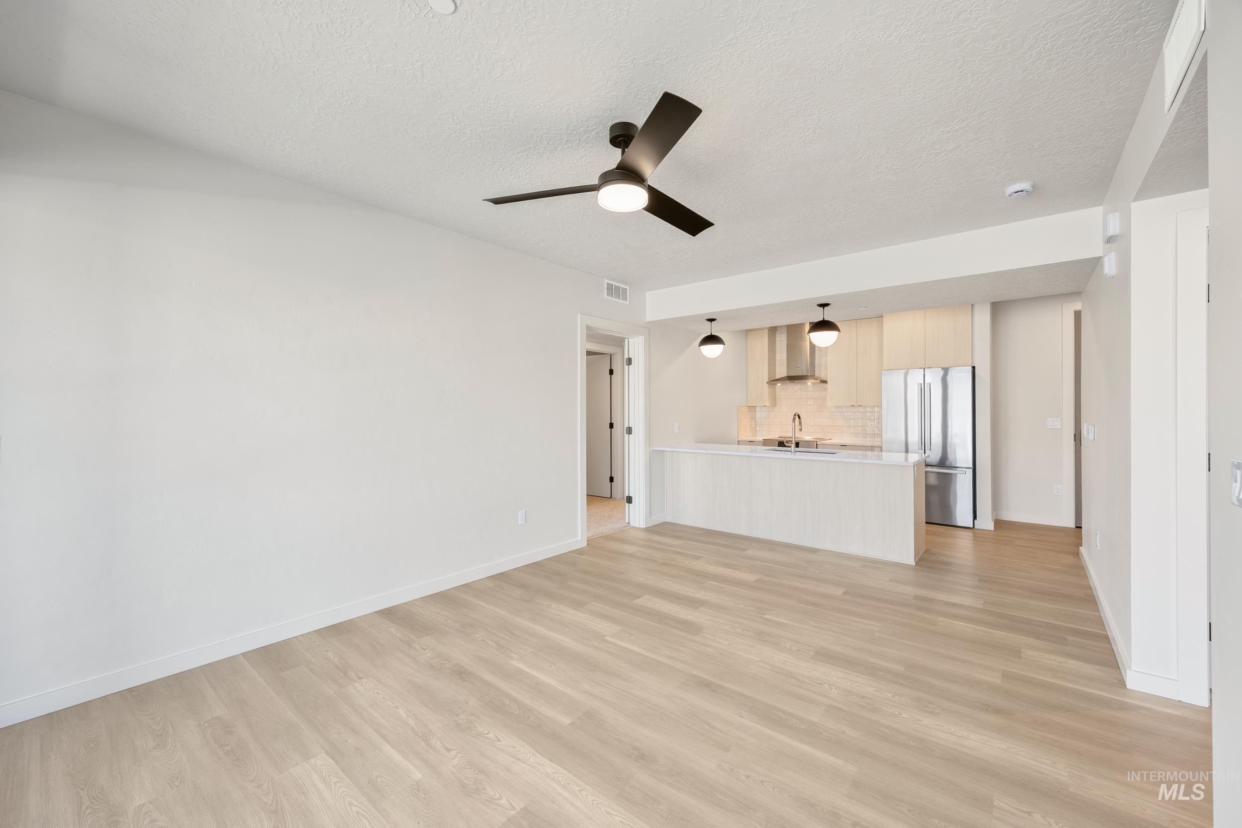 Unfurnished living room with light wood finished floors, ceiling fan, and a textured ceiling