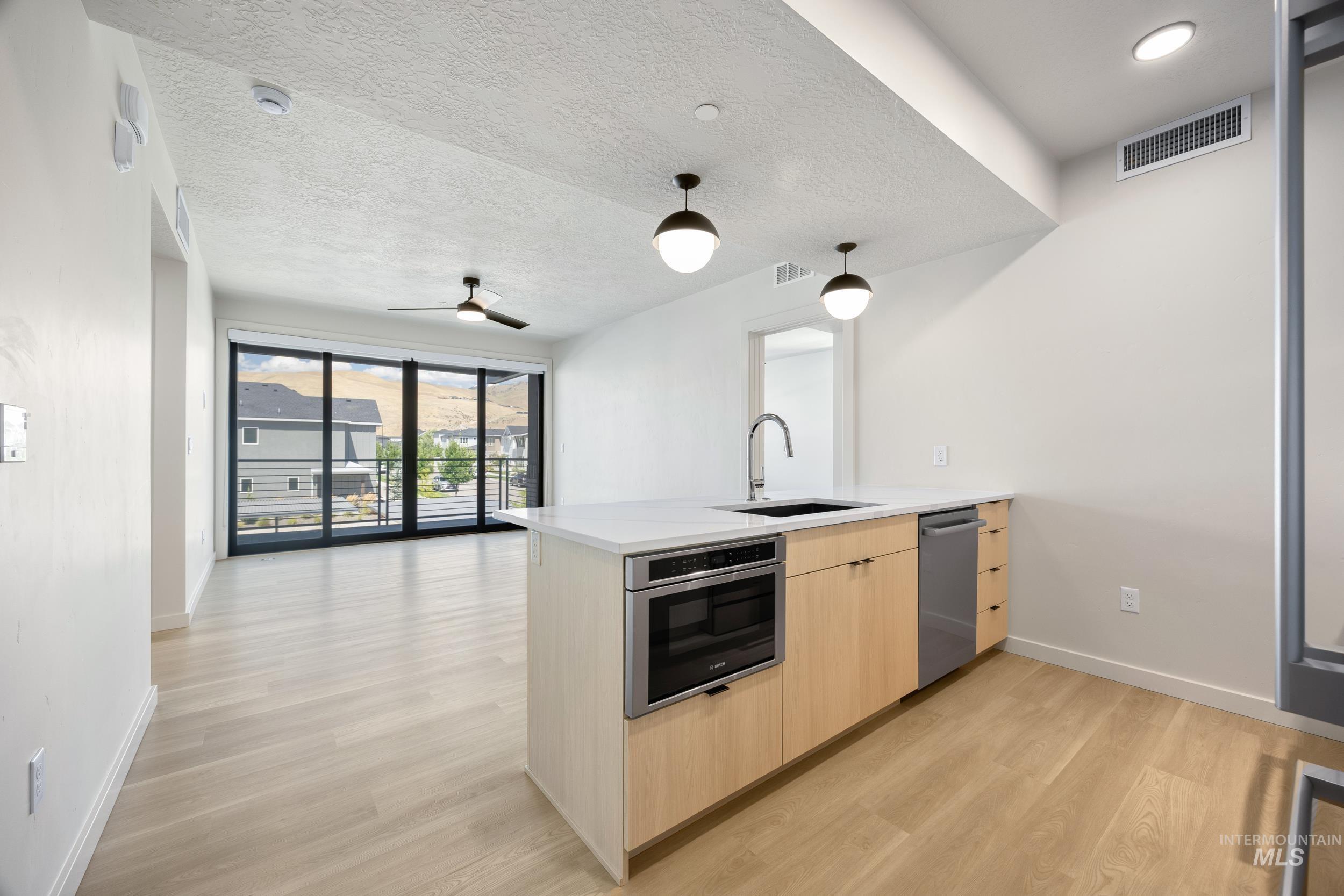 Kitchen with light brown cabinets, a peninsula, decorative light fixtures, light stone counters, and modern cabinets