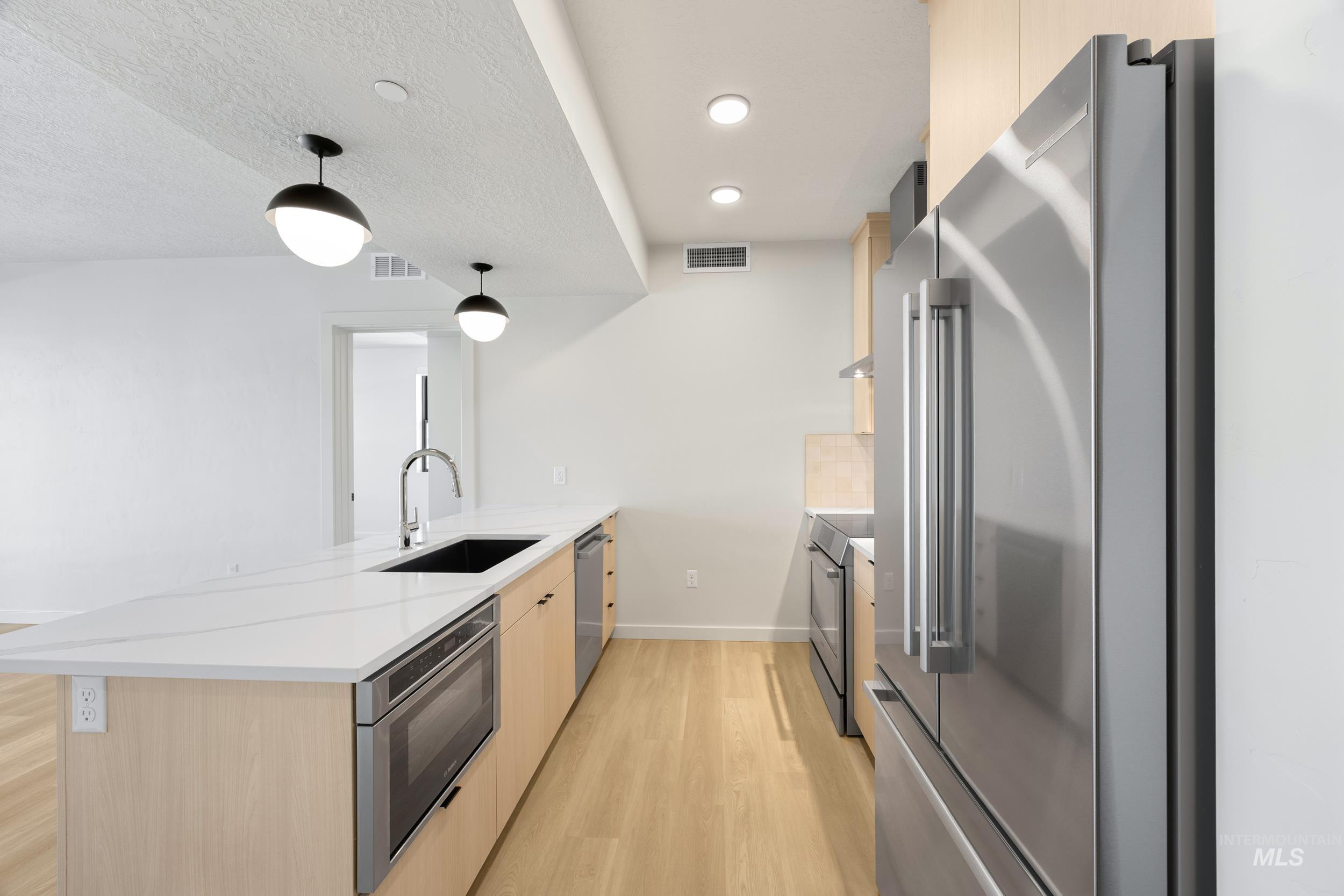 Kitchen with light brown cabinets, a peninsula, stainless steel appliances, light wood-type flooring, and modern cabinets
