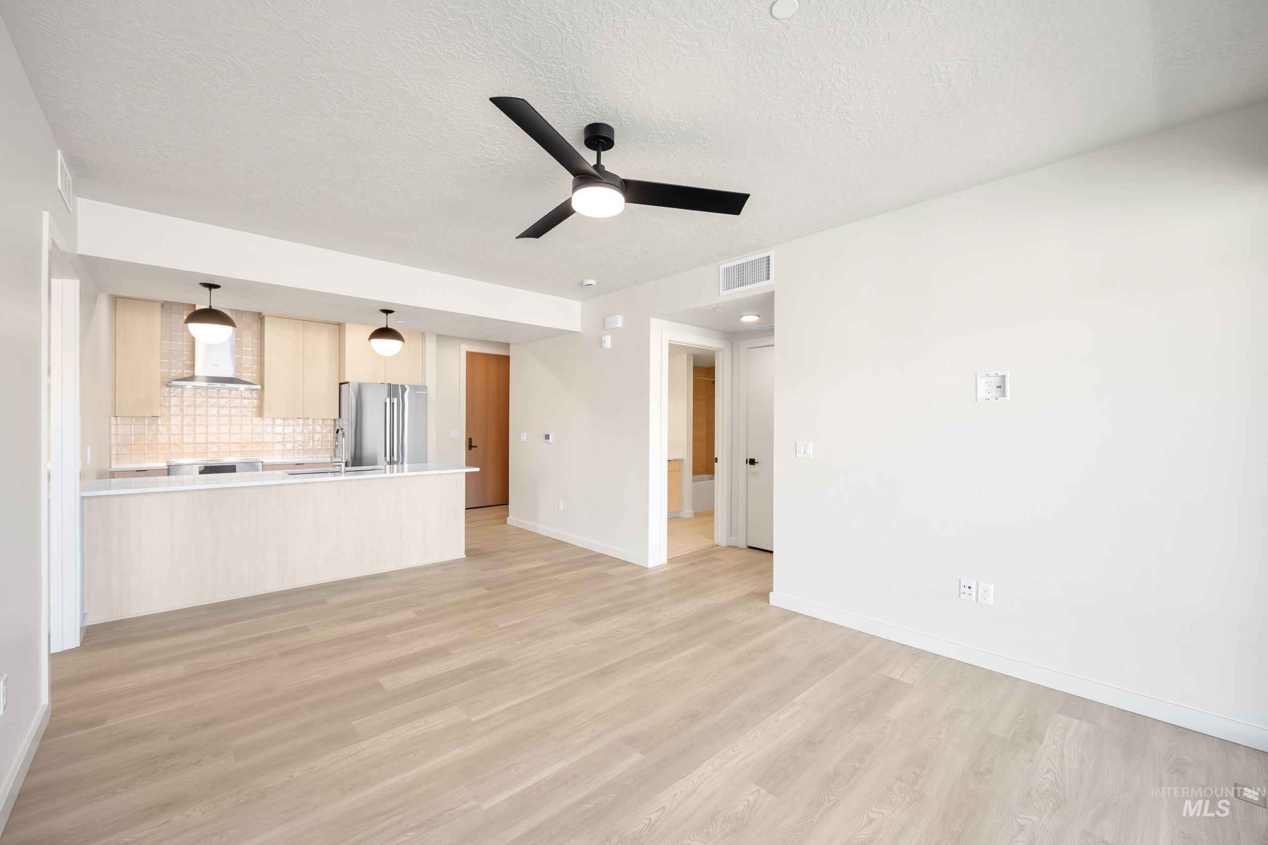 Unfurnished living room featuring ceiling fan, light wood-style flooring, and a textured ceiling