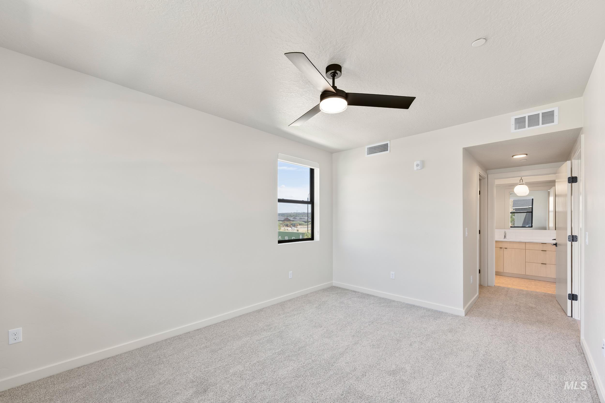 Unfurnished bedroom with light colored carpet, a ceiling fan, connected bathroom, and a textured ceiling