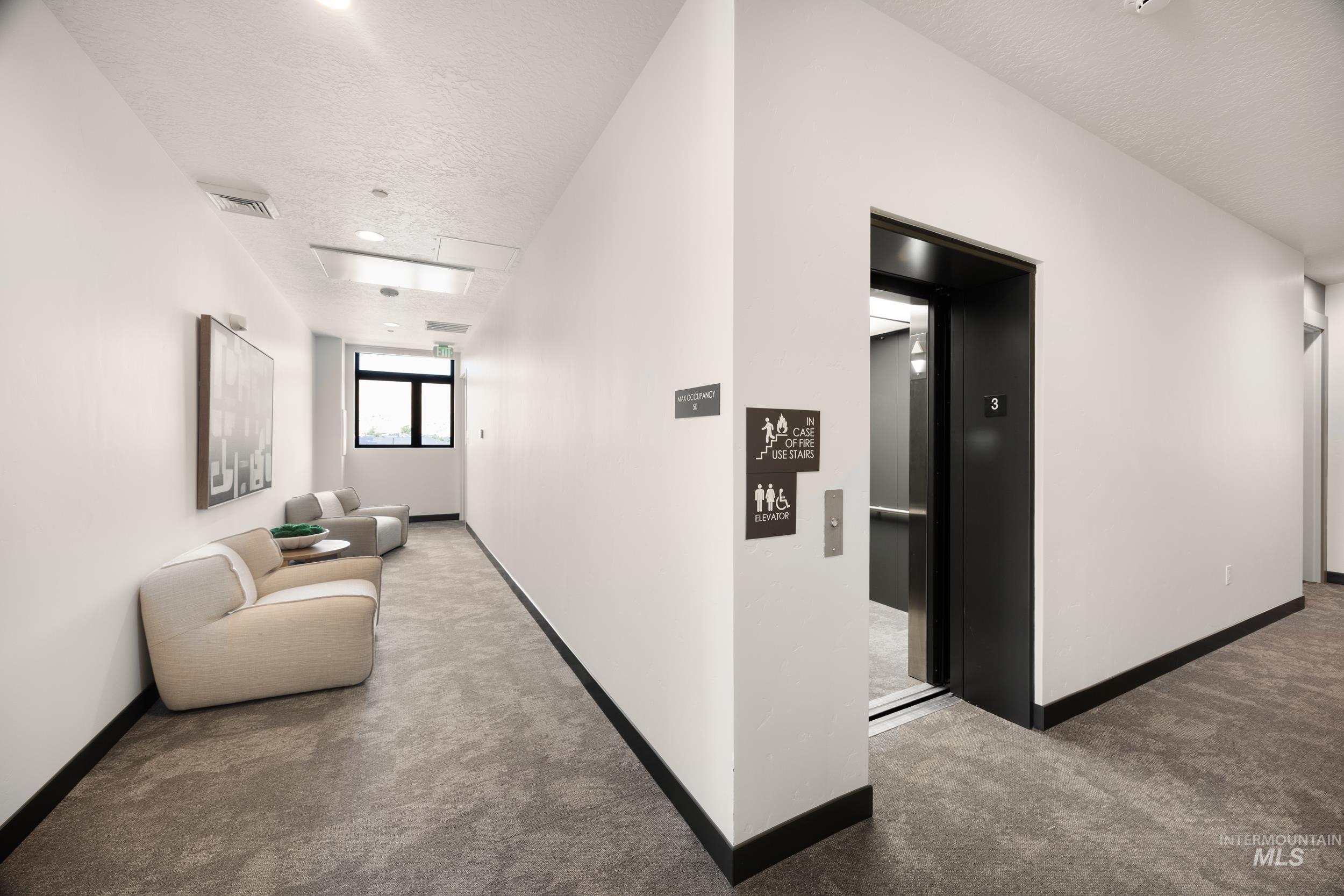 Hall featuring carpet floors, a textured ceiling, and elevator