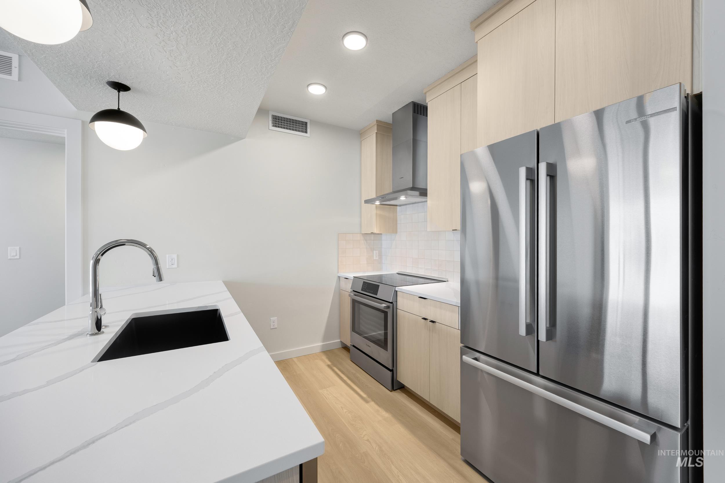 Kitchen with appliances with stainless steel finishes, light wood-style flooring, modern cabinets, light stone countertops, and recessed lighting
