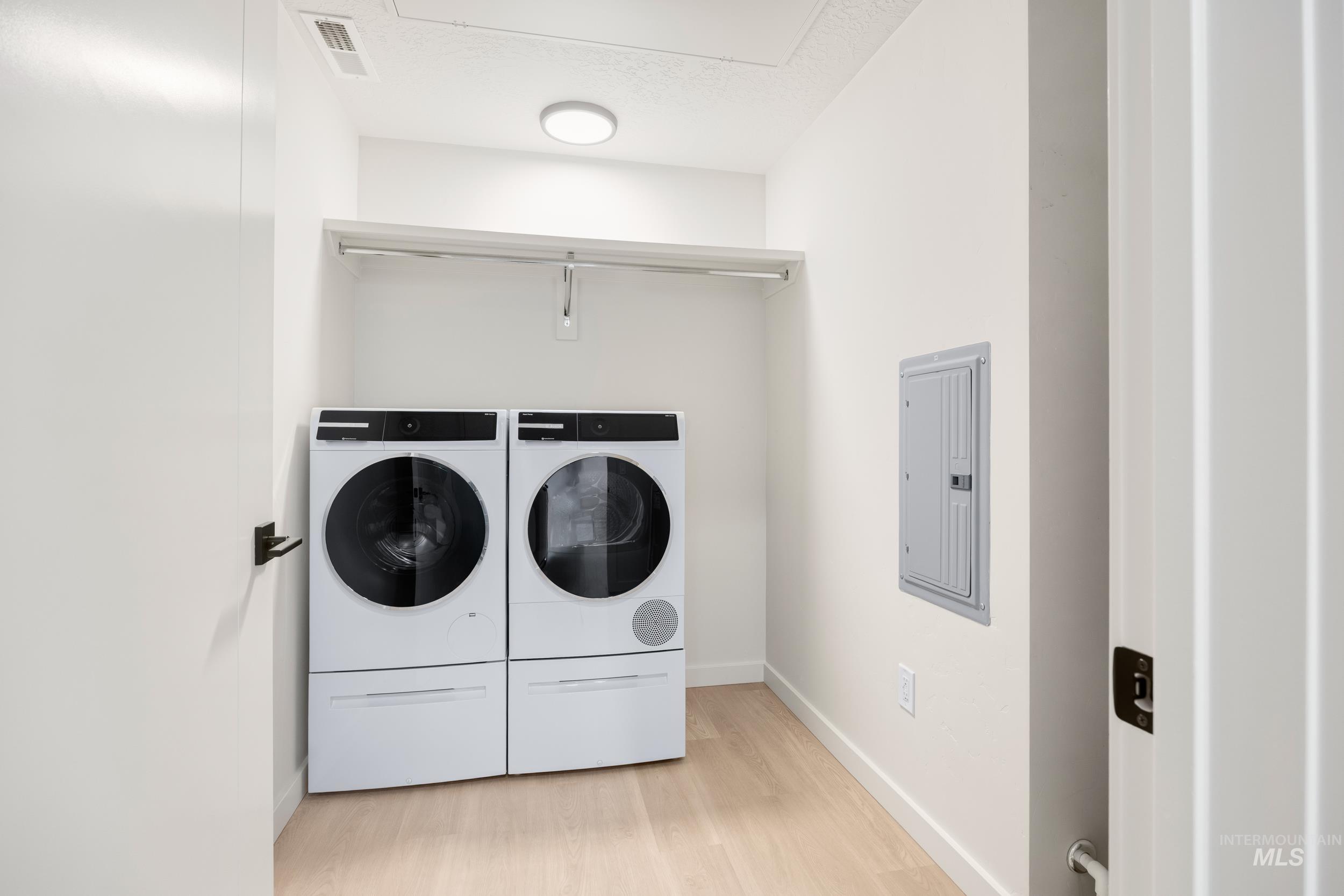 Washroom featuring light wood-type flooring, electric panel, washing machine and clothes dryer, and a textured ceiling