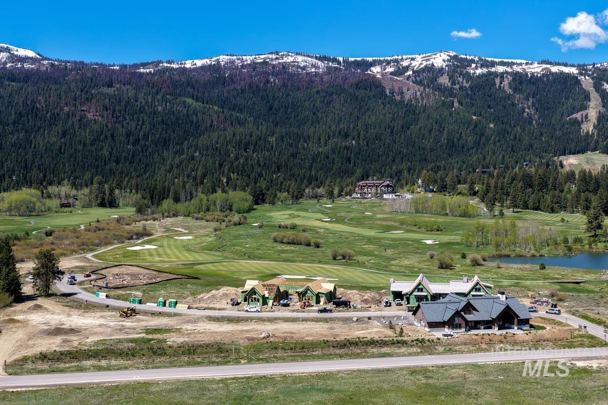 New construction homes situated alongside a golf course, surrounded by mature conifer forests and snow-capped mountains