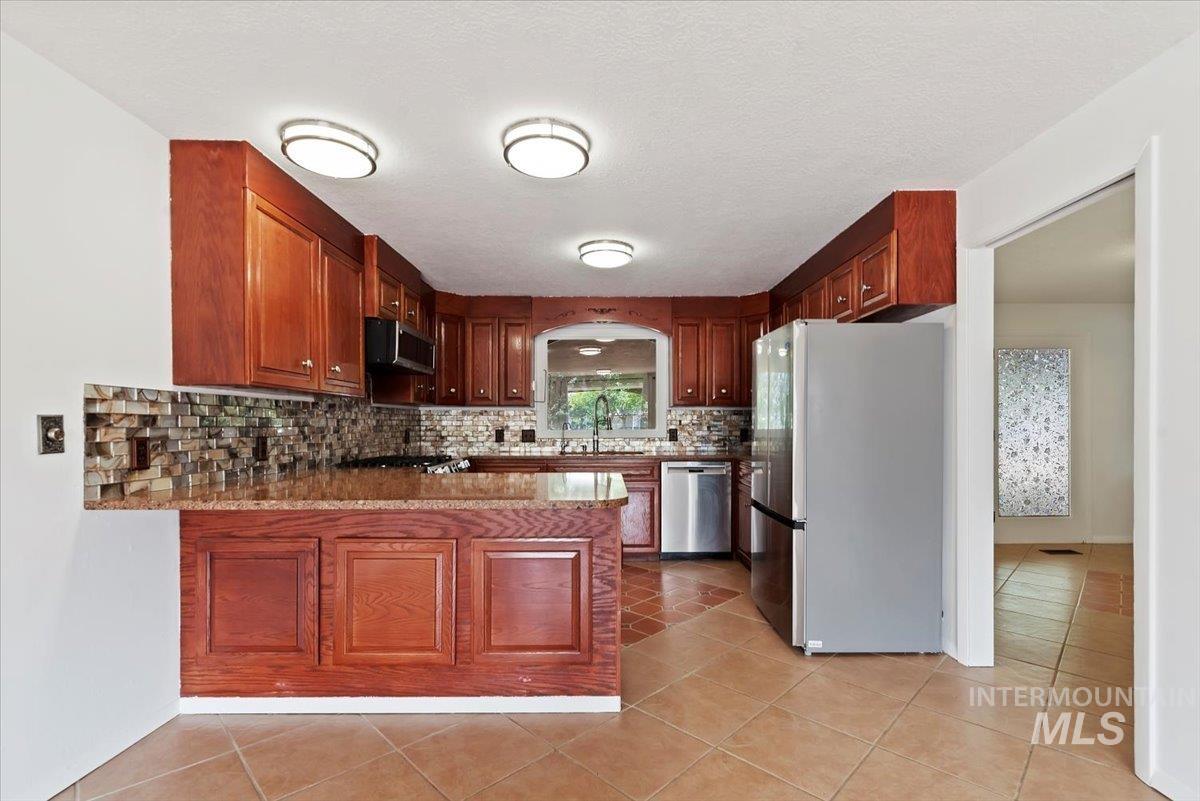 Kitchen with stainless steel appliances, light stone countertops, light tile patterned floors, a peninsula, and a textured ceiling