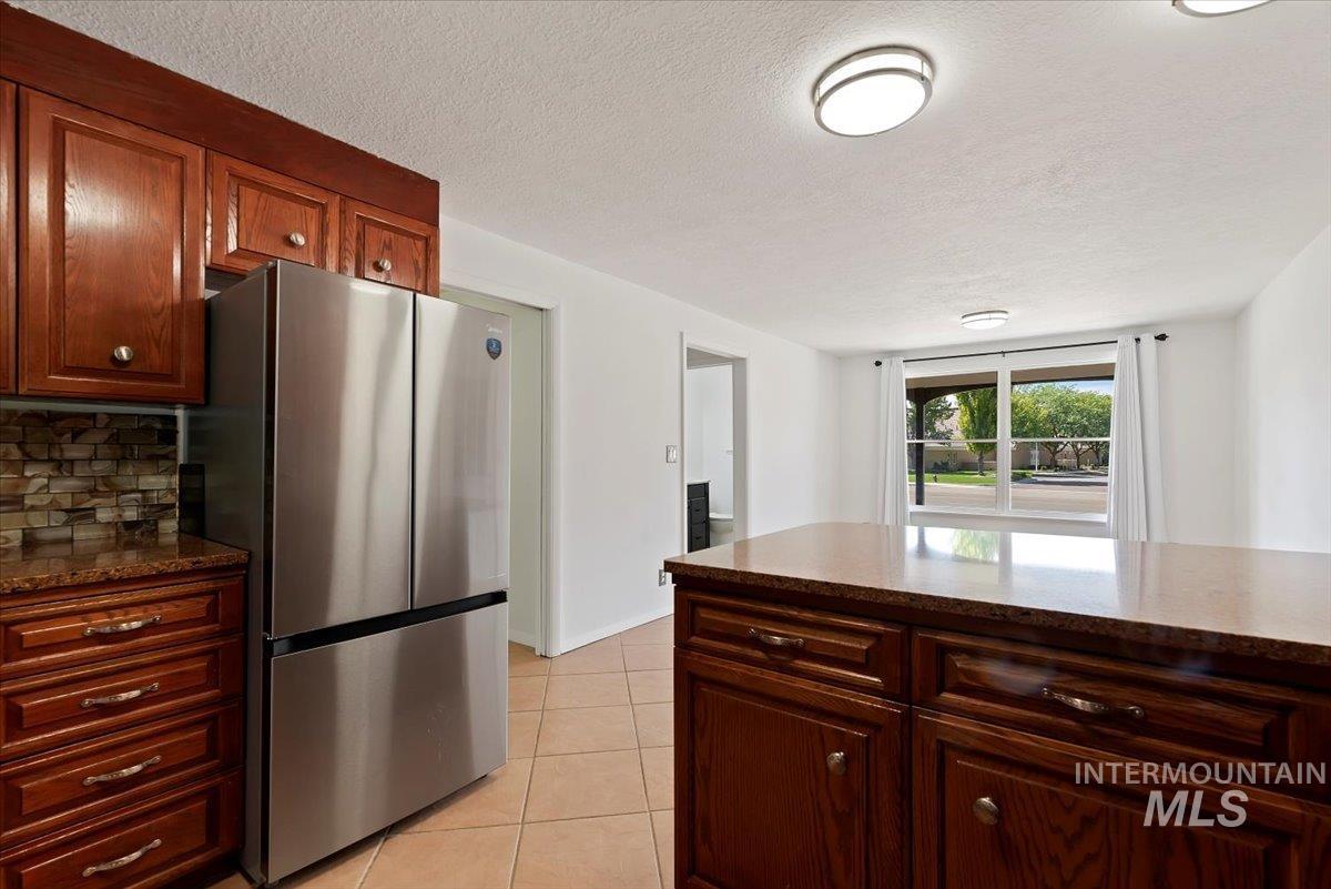 Kitchen featuring freestanding refrigerator, dark stone countertops, light tile patterned flooring, a textured ceiling, and decorative backsplash
