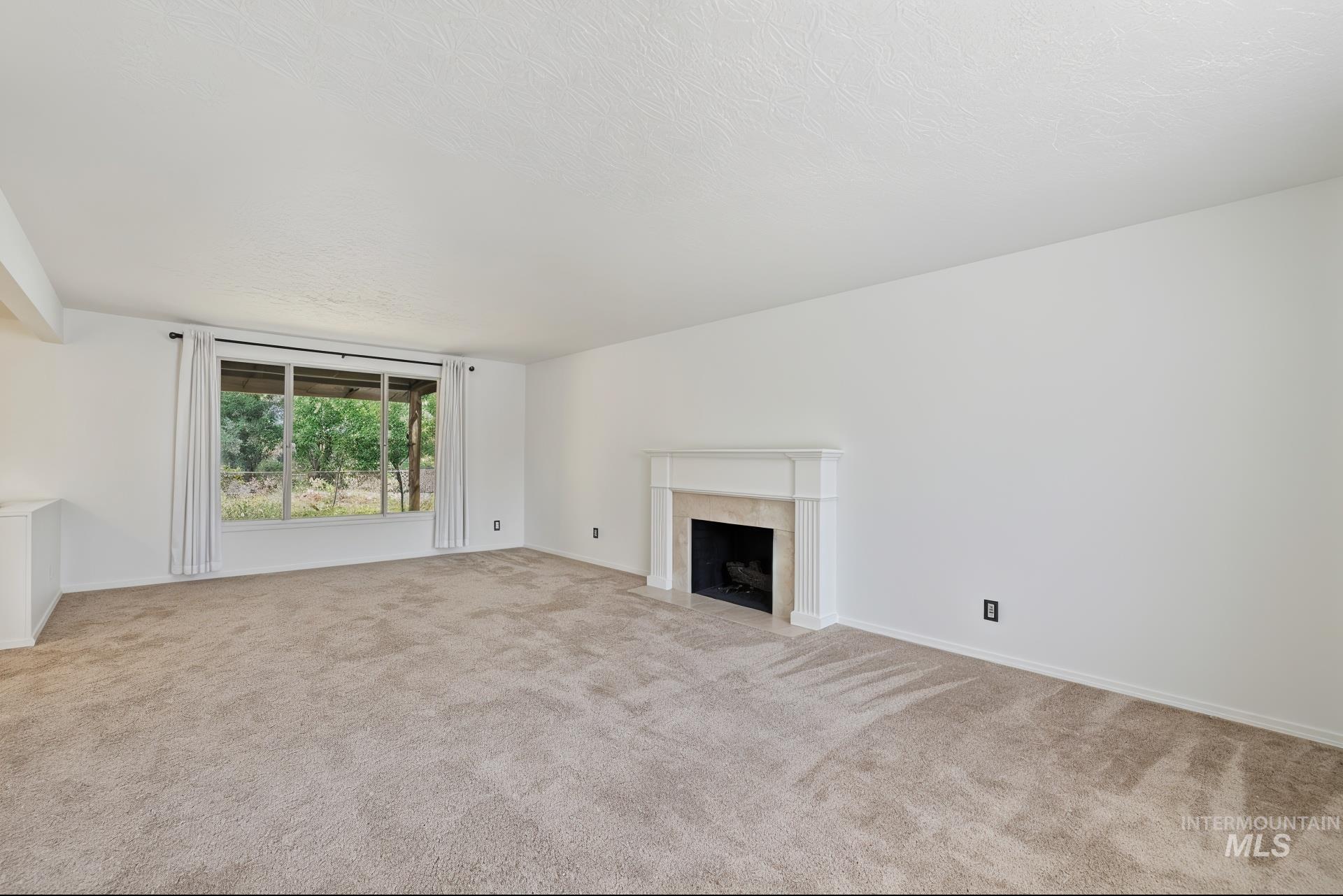 Unfurnished living room featuring light carpet, a high end fireplace, and a textured ceiling