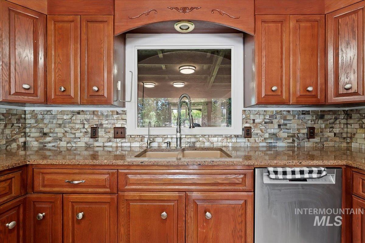 Kitchen with brown cabinets, dishwasher, and light stone counters