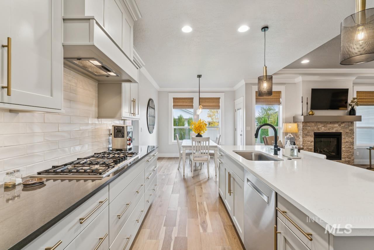 Kitchen with decorative light fixtures, light stone countertops, light wood-style flooring, white cabinets, and ornamental molding