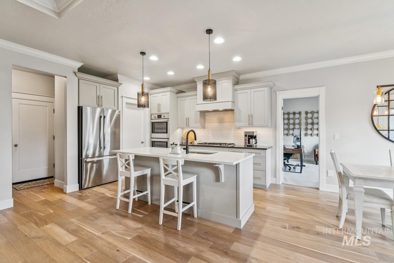 Kitchen with ornamental molding, appliances with stainless steel finishes, a breakfast bar area, pendant lighting, and backsplash