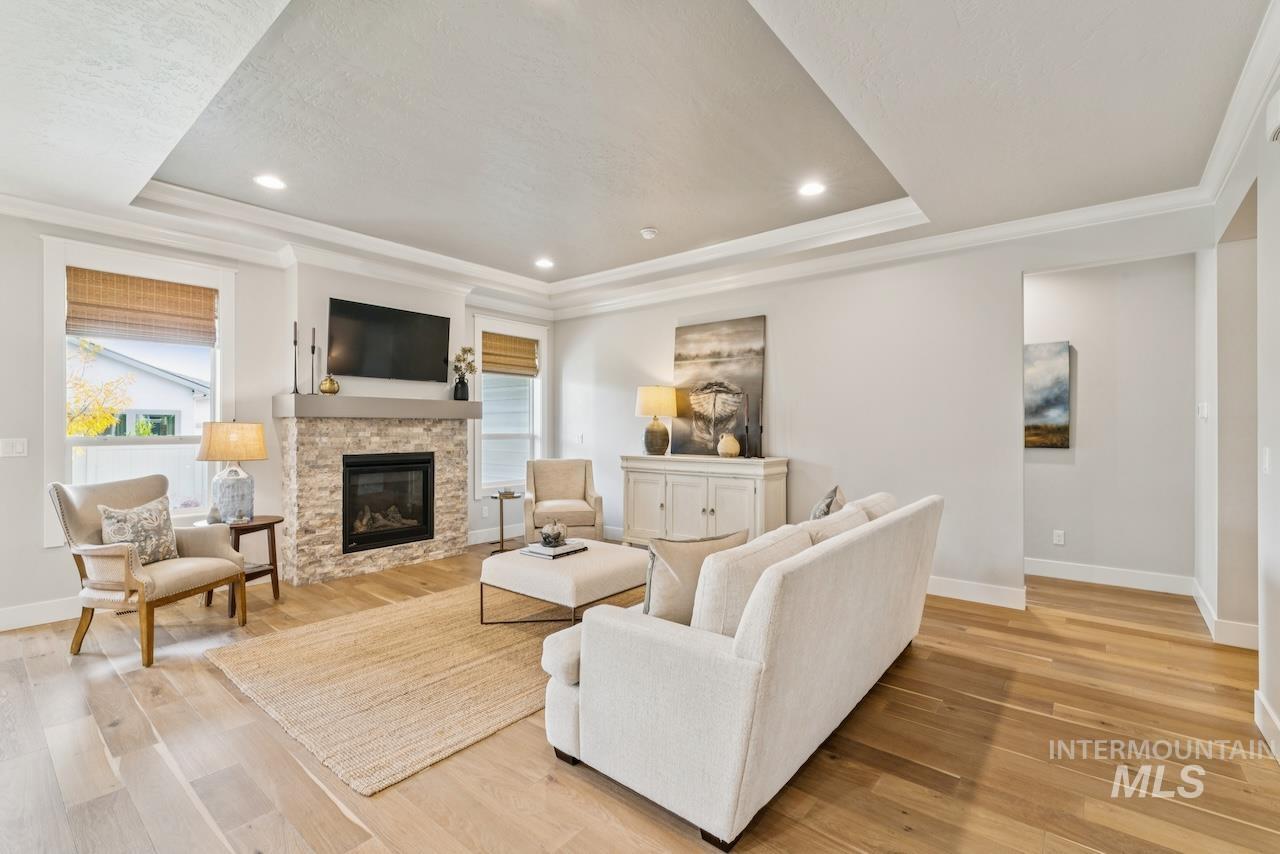 Living room featuring recessed lighting, light wood-style flooring, a tray ceiling, crown molding, and a fireplace
