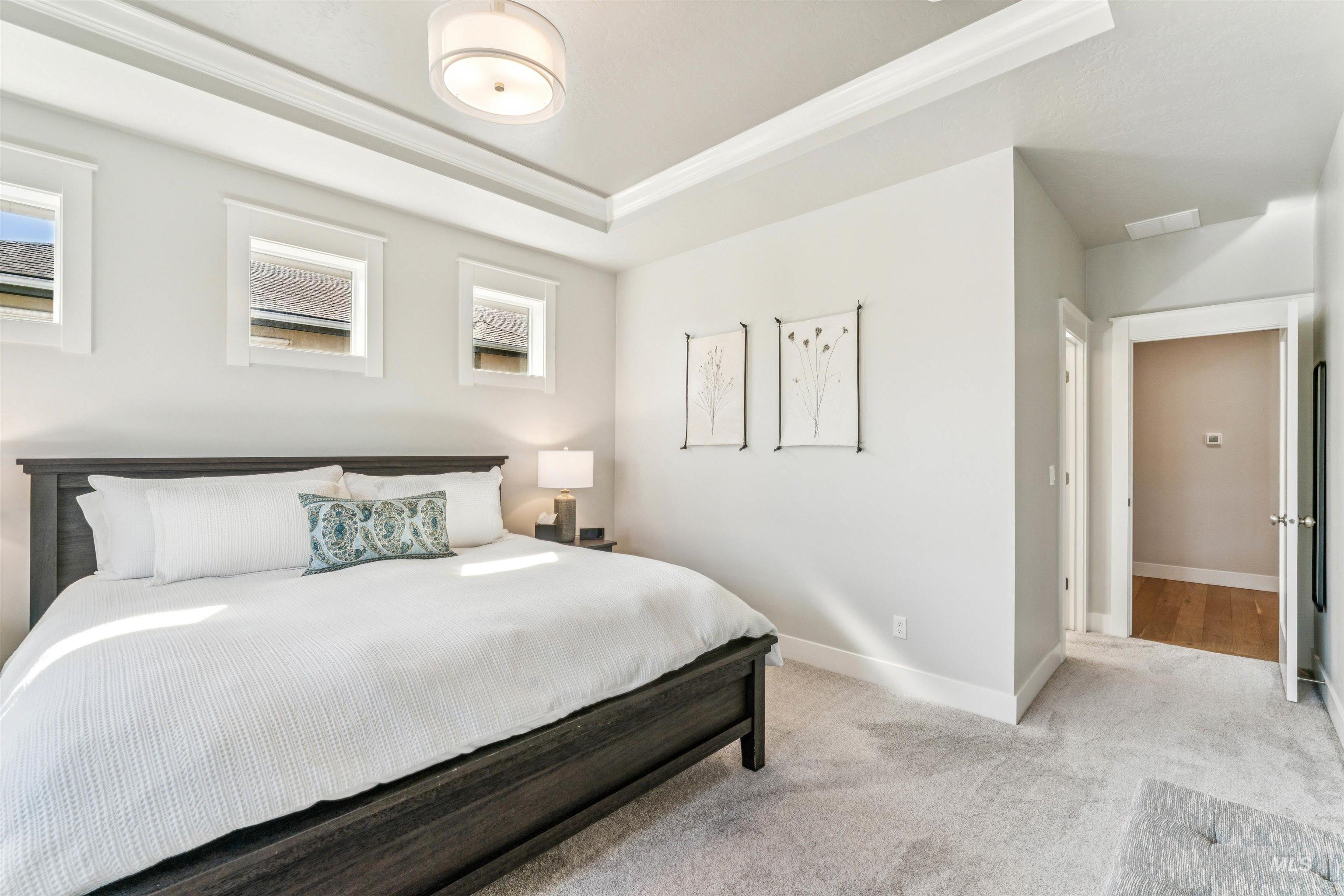 Bedroom with light carpet, a raised ceiling, and crown molding